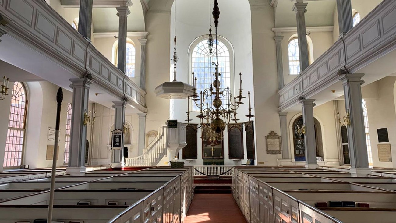 Interior of church looking down center aisle with white box pews on either side.