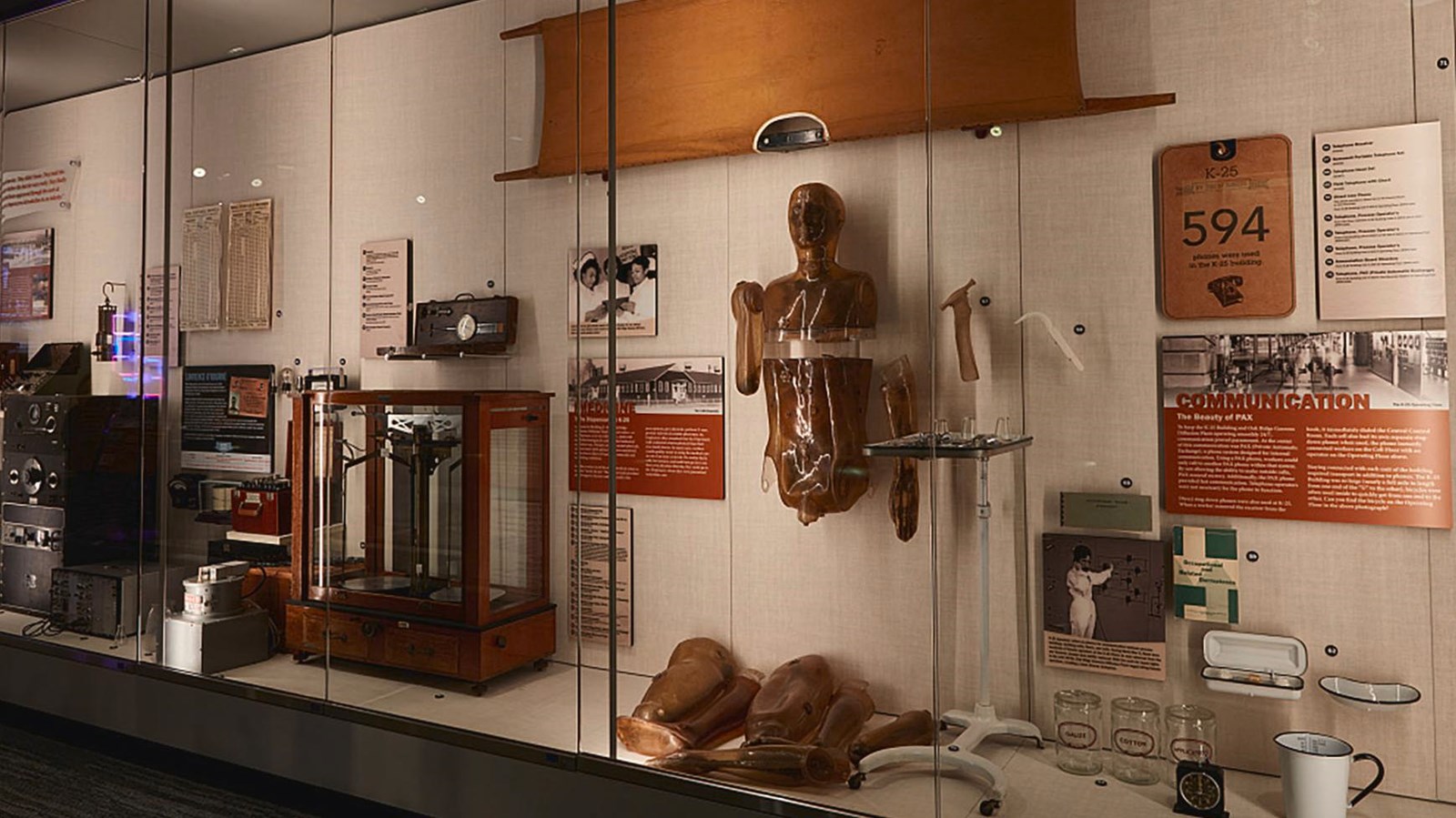 A stretcher, manniquen, medical, and scientific equipment displayed in glass cases along a wall