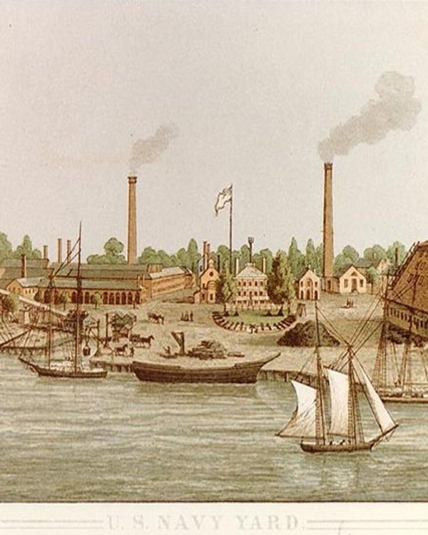 Washington Navy Yard in the 1800s. There are ships on the water and smokestacks in the background.