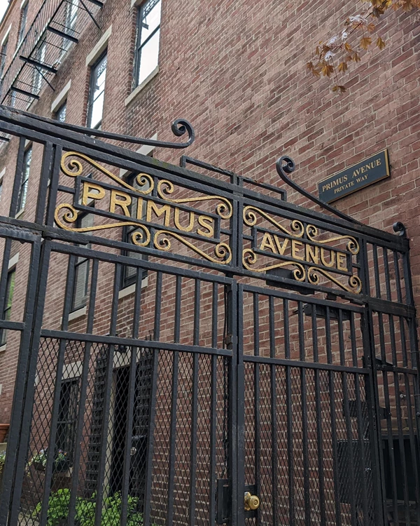 a black iron gate with the words primus avenue sits at the entrance of an brick lined alley