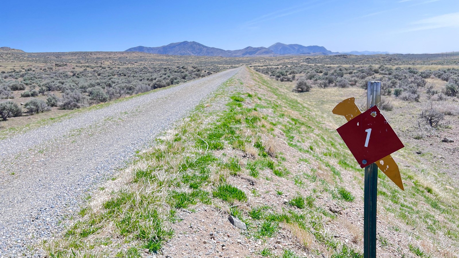 Gravel road, low mountain in distance, diamond brown shape and golden spike marker