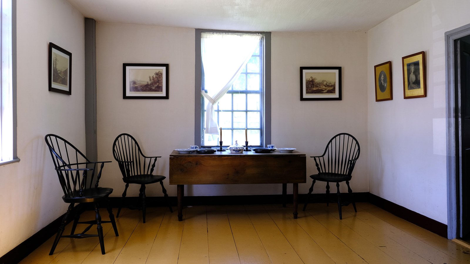 Plain room with dining table, chairs, and several landscape paintings. 