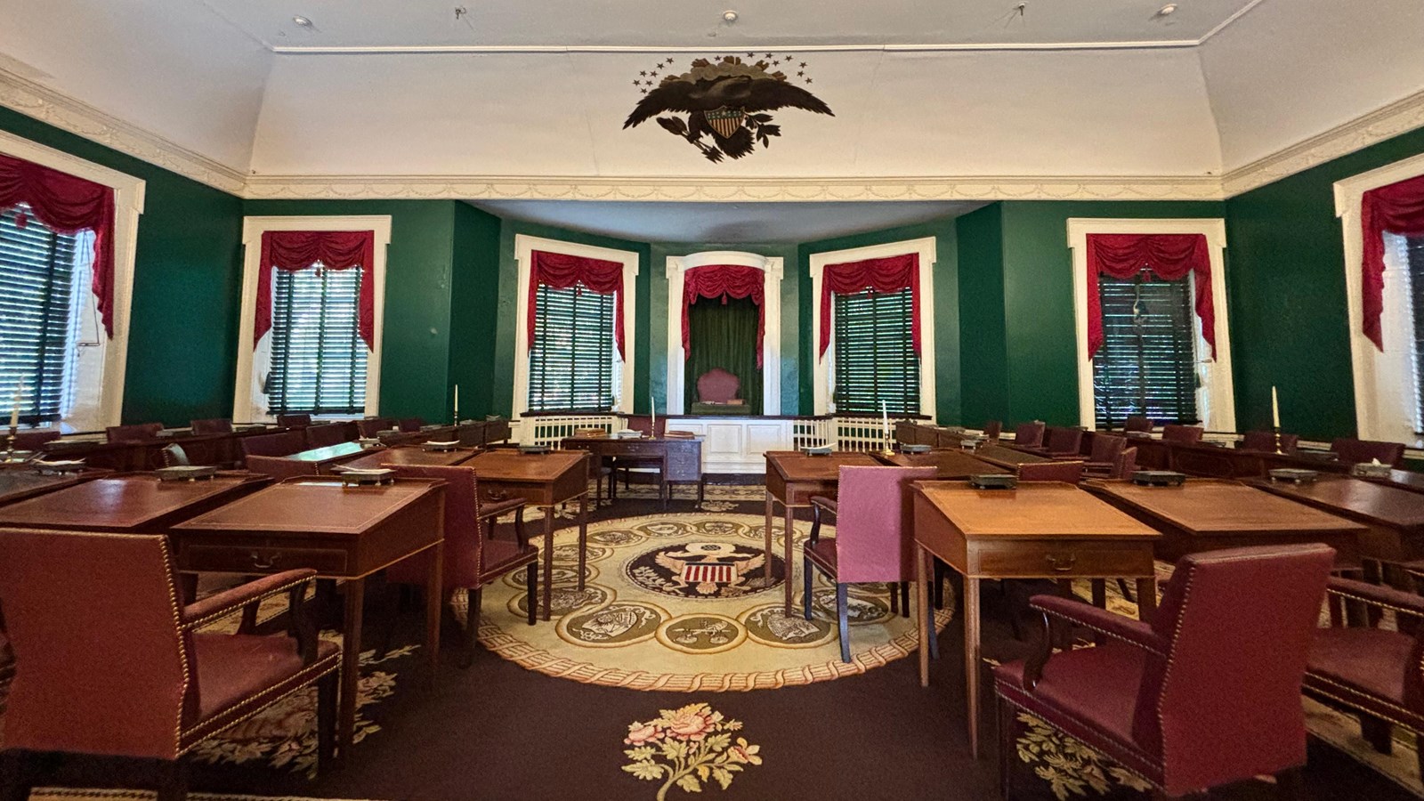 A green room with many chairs and desks, a colorful carpet and curtains
