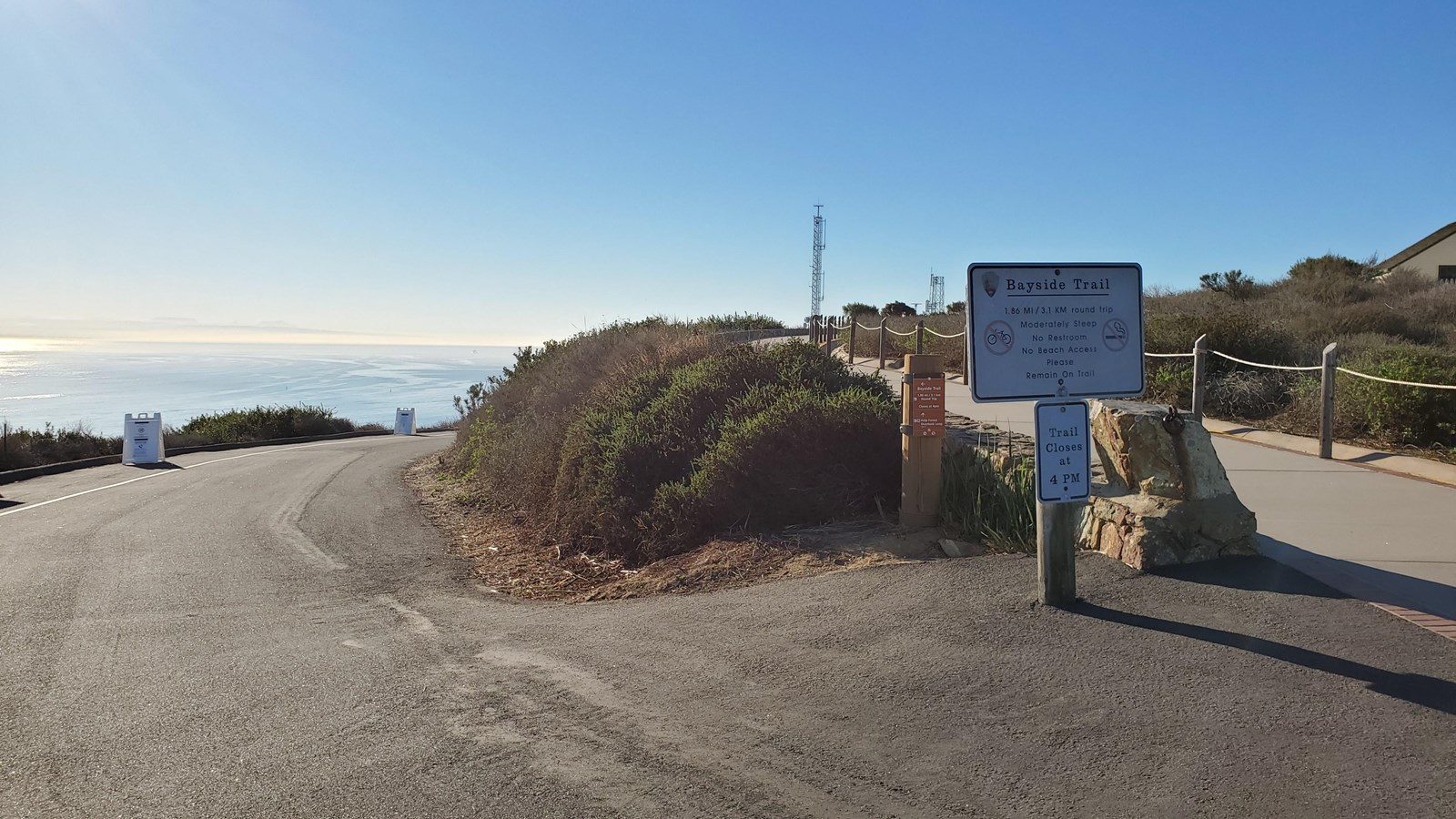 A black asphalt road curves downhill past a white sign that reads