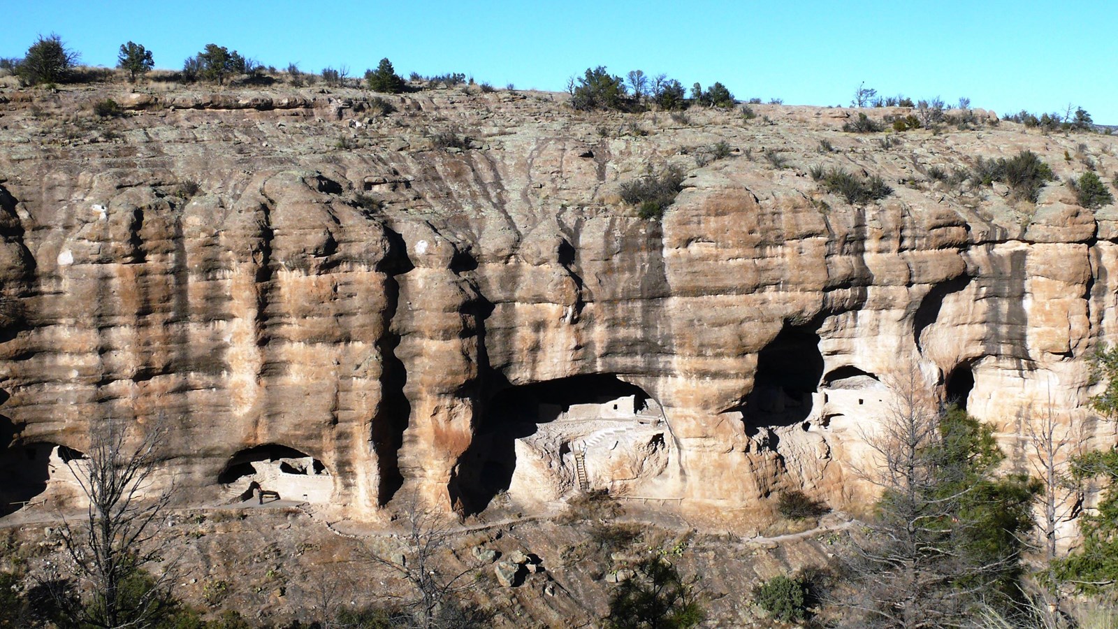 A pink rock face with black streaks with 3 caves with stone stacked structures. 