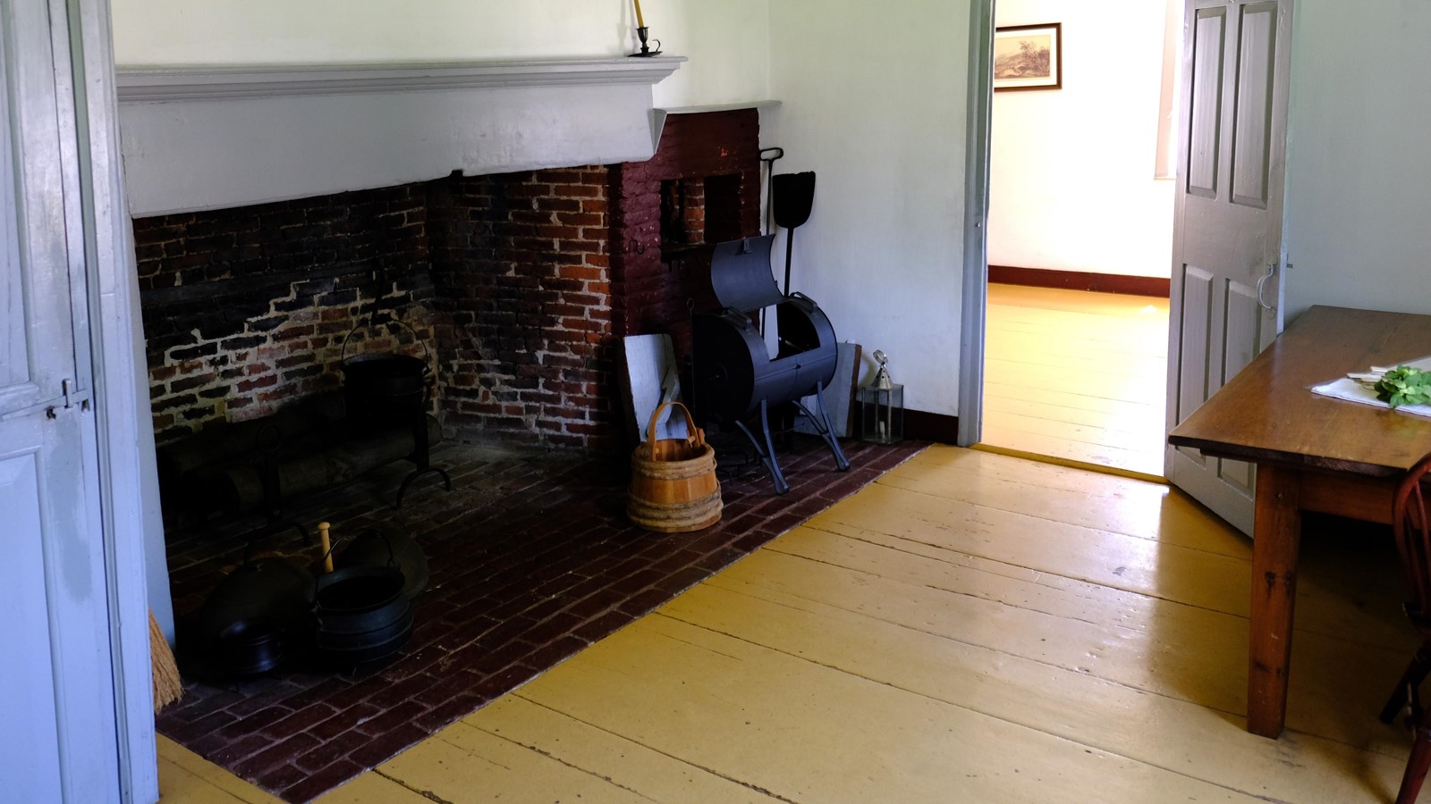 A partial view of a room with a large fireplace and cooking tools.