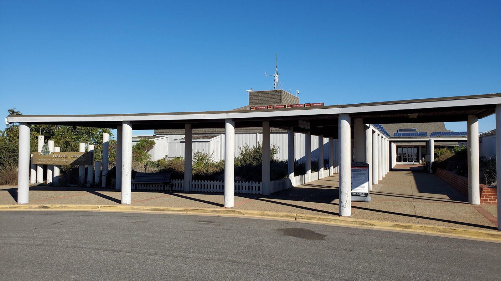 Cylindrical white pillars hold up a dark-brown roof to shade gray sidewalk.