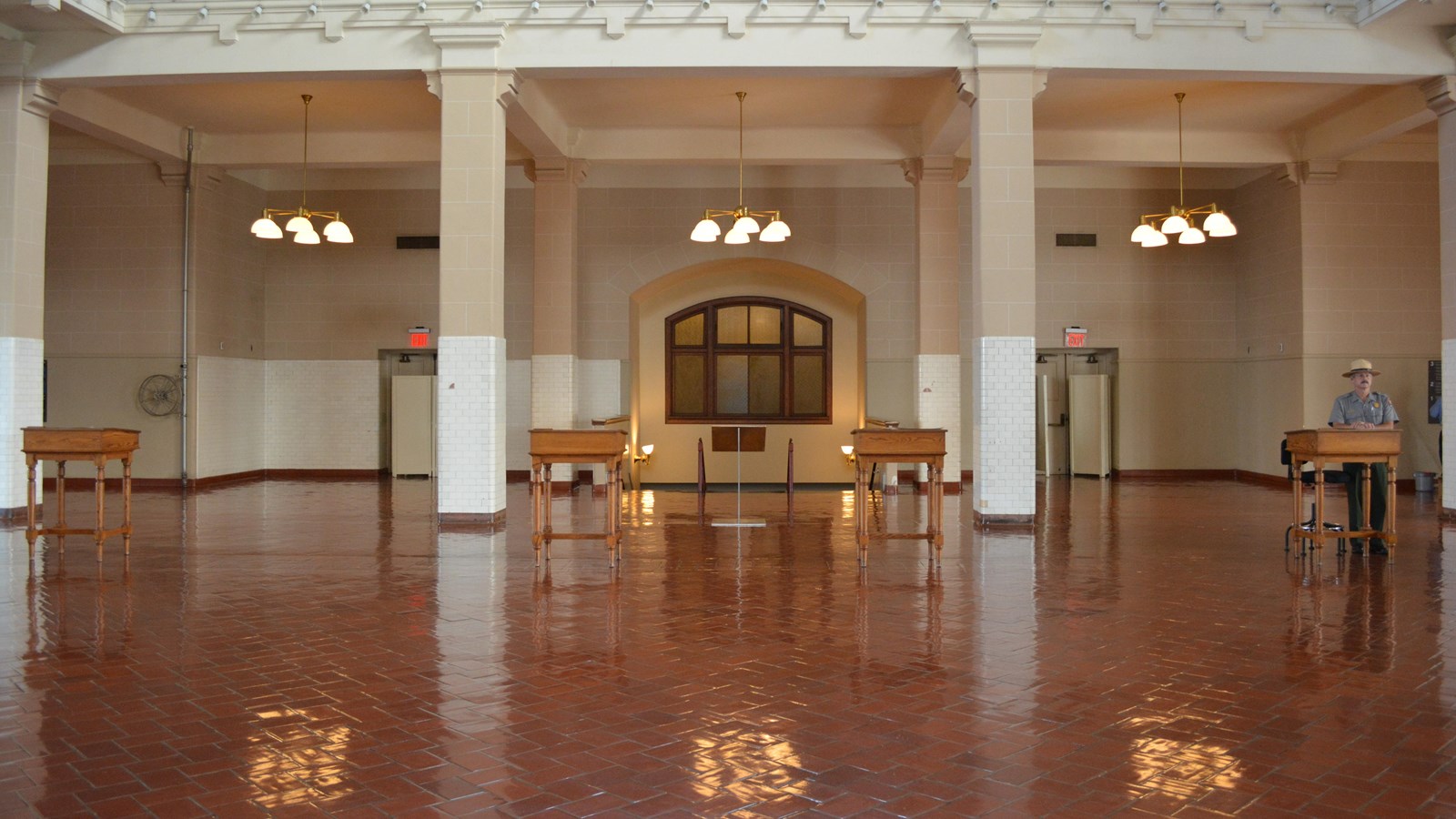 Four waist high desks equally spaced across a dark red floor reflecting three hanging light fixtures