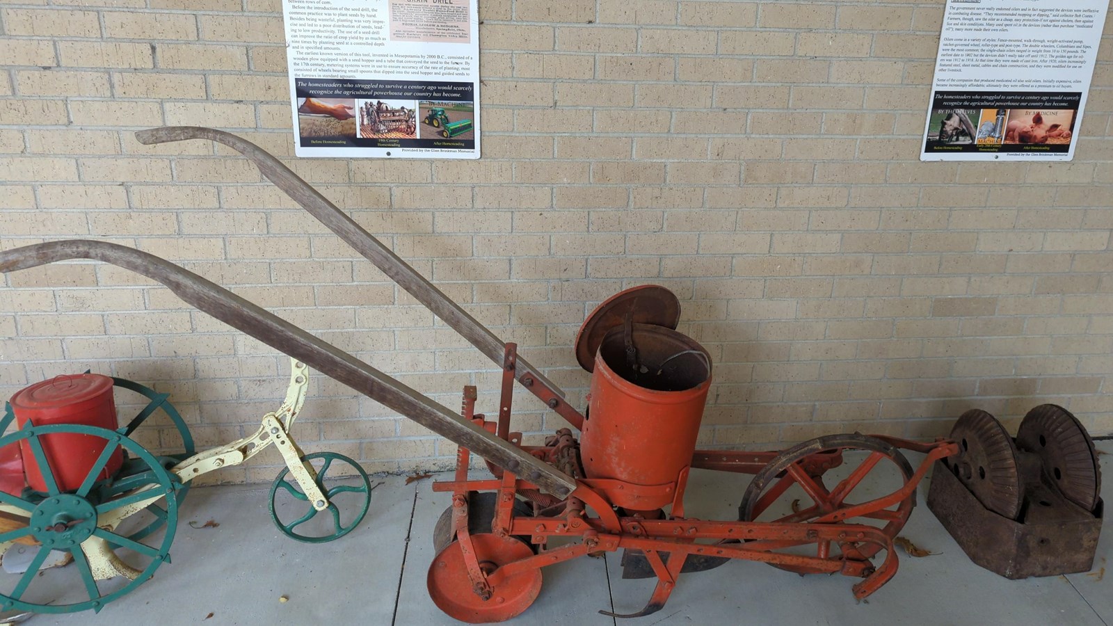 Machine with rakes to dig furrows and a can to hold seed next to a metal wheel used to oil hogs.