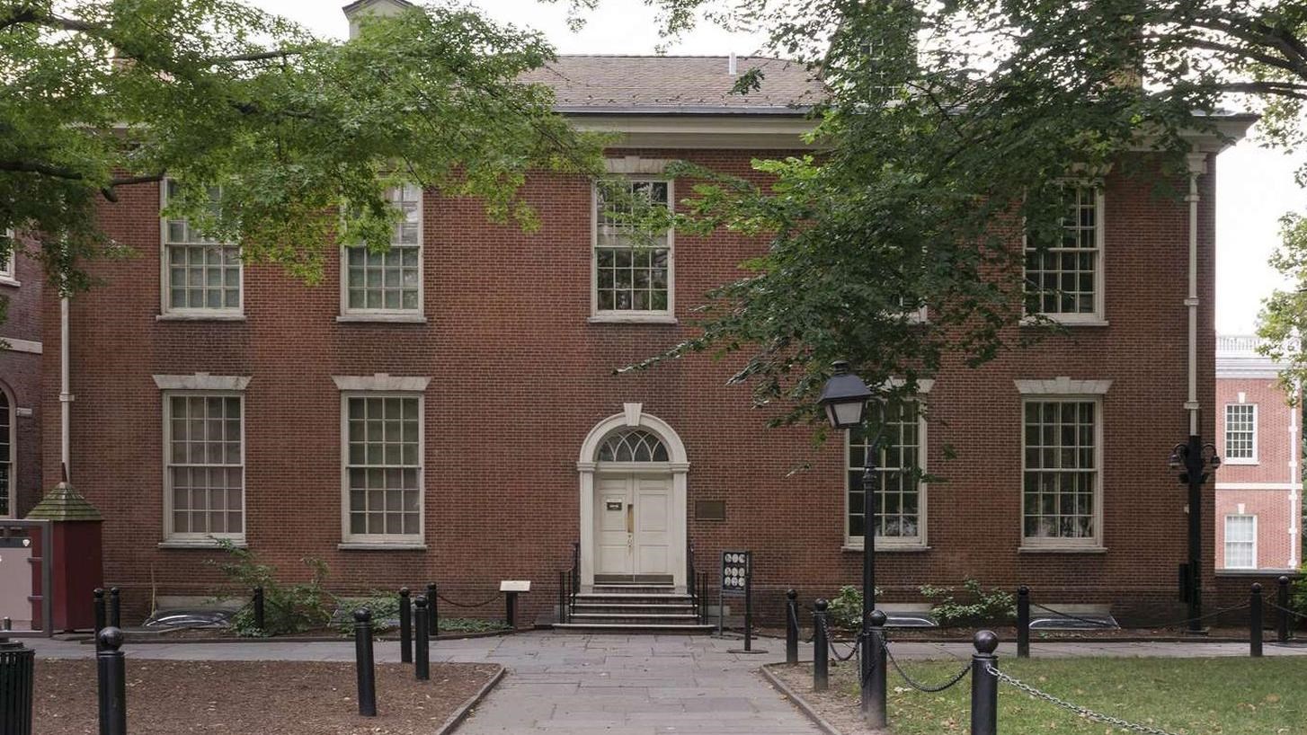 A color photo of a two story brick building with a concrete path leading to a front white door.
