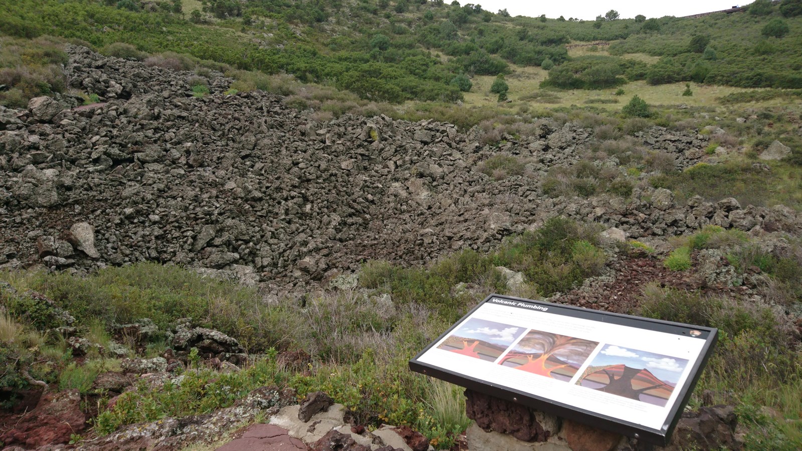 Sign on the right with basalt lava rocks at the bottom of the crater at Capulin Volcano
