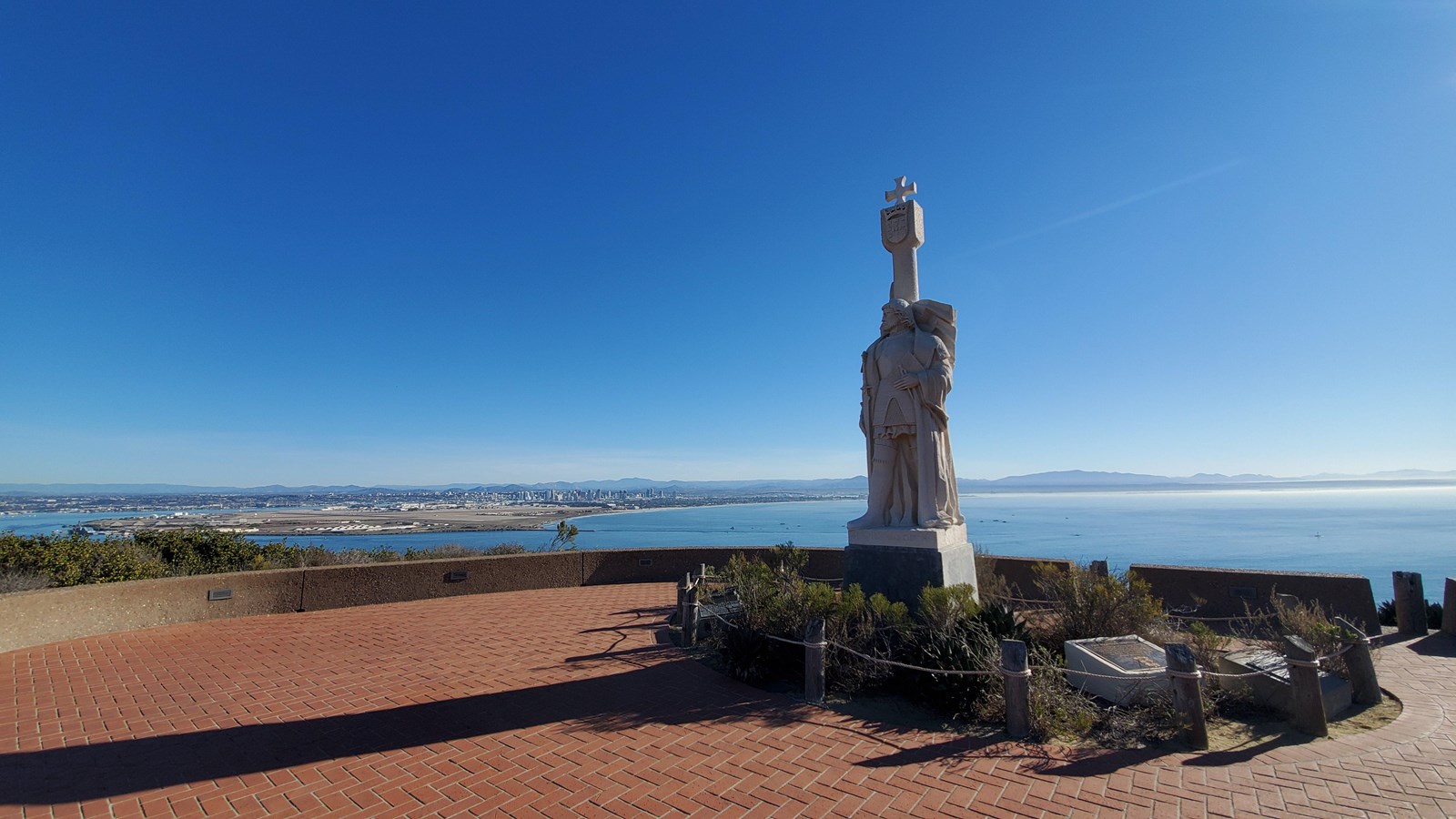 Sandy-white stone statue of the man Cabrillo in the center of a circular brick plaza.