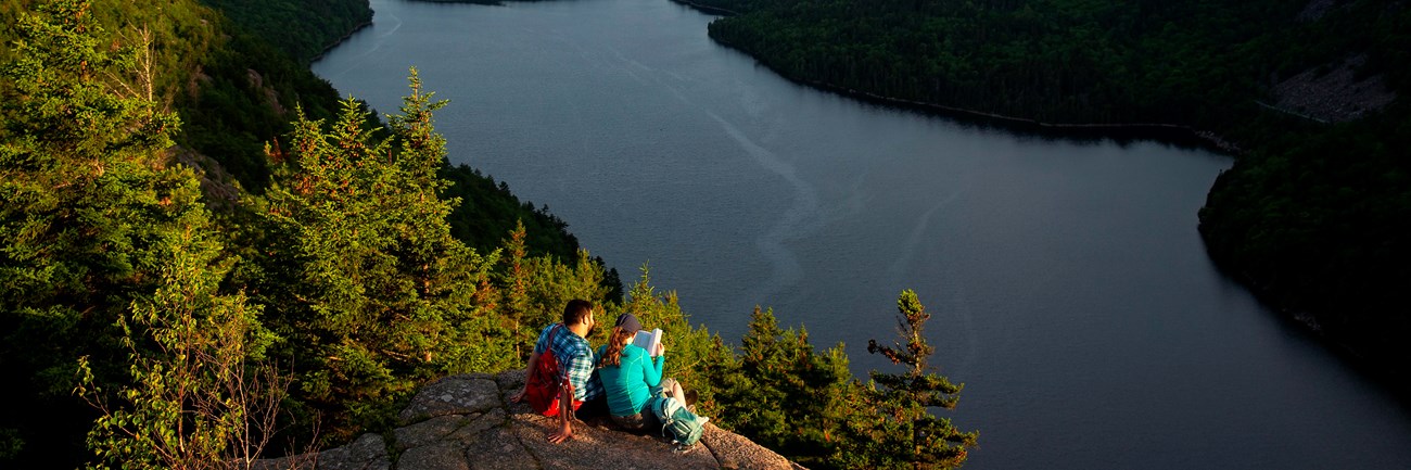Visitors sitting on a rock ledge overlooking a lake