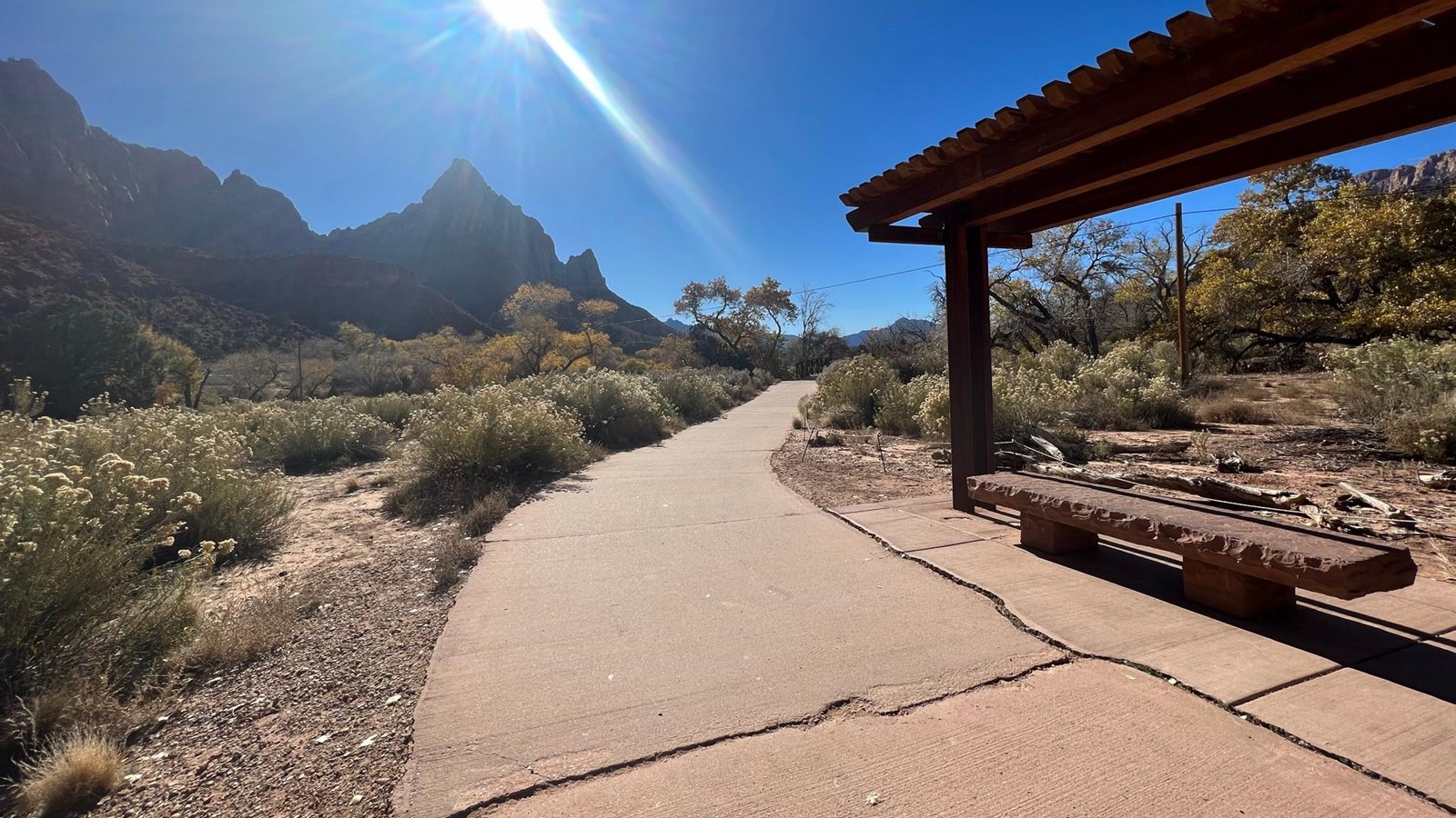 Photo of a paved path bending around a shade structure towards a mountain