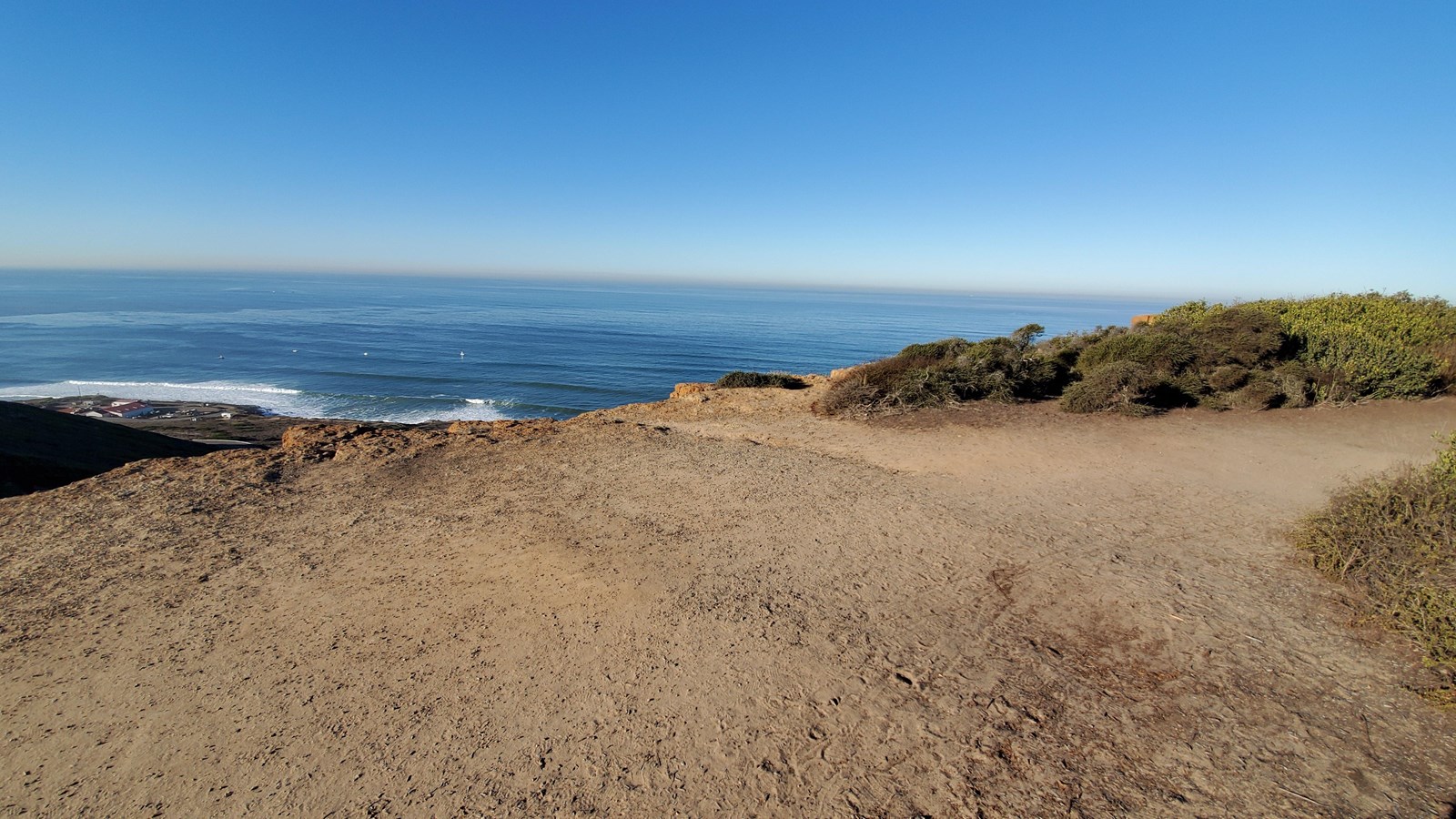 A sandy path clearing overlooks blue waters.