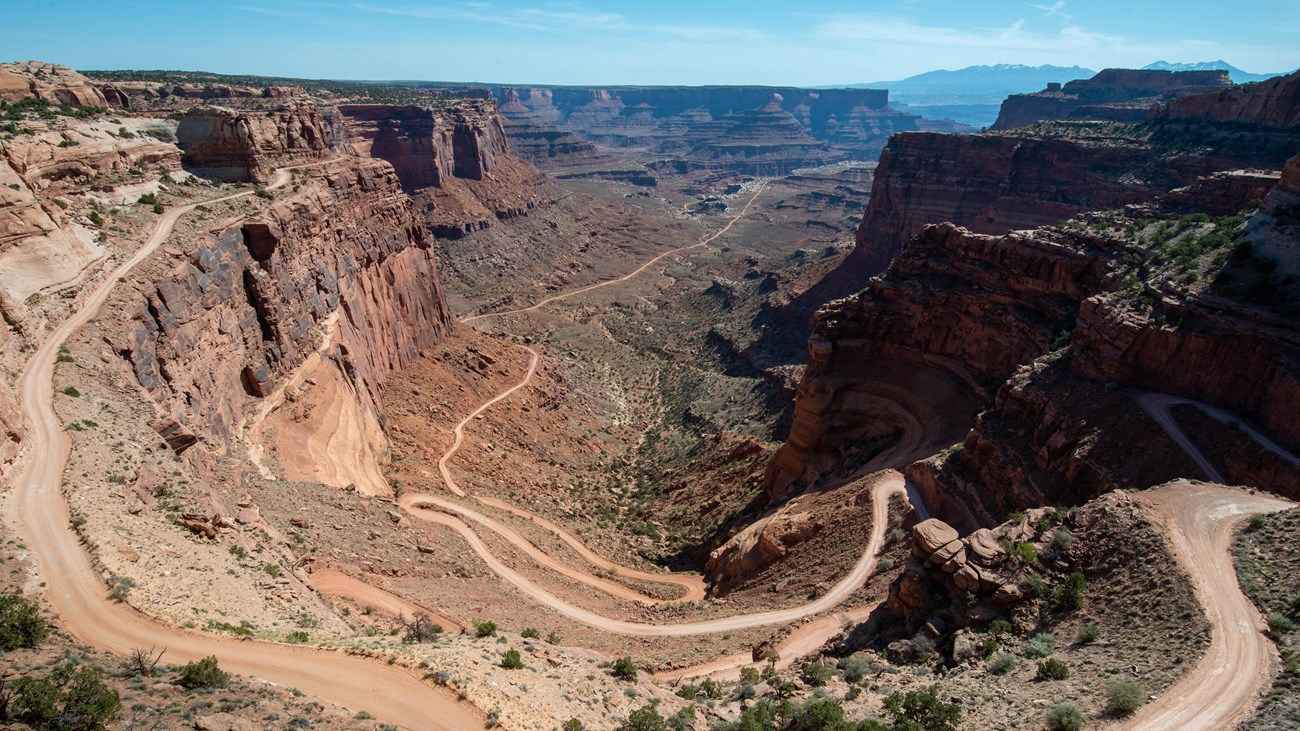 A light beige unpaved road winds back and forth down colorful sandstone walls.