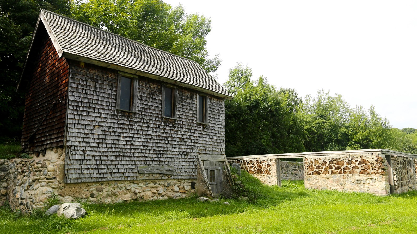 Two-story, shingle-sided building with a tall stone foundation and a bright green lawn