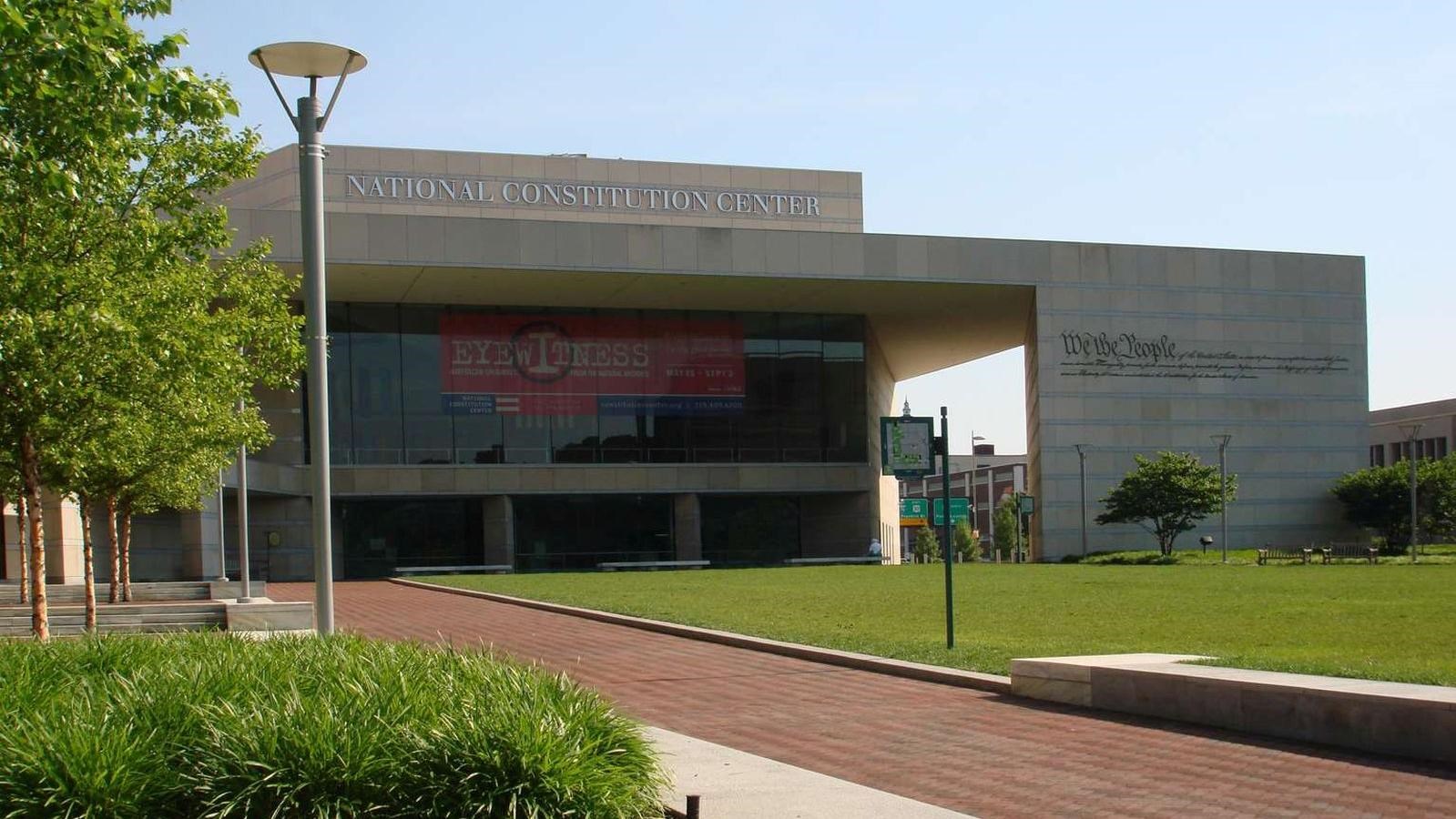 A color photo showing a brick path leading to a modern gray building with large windows.