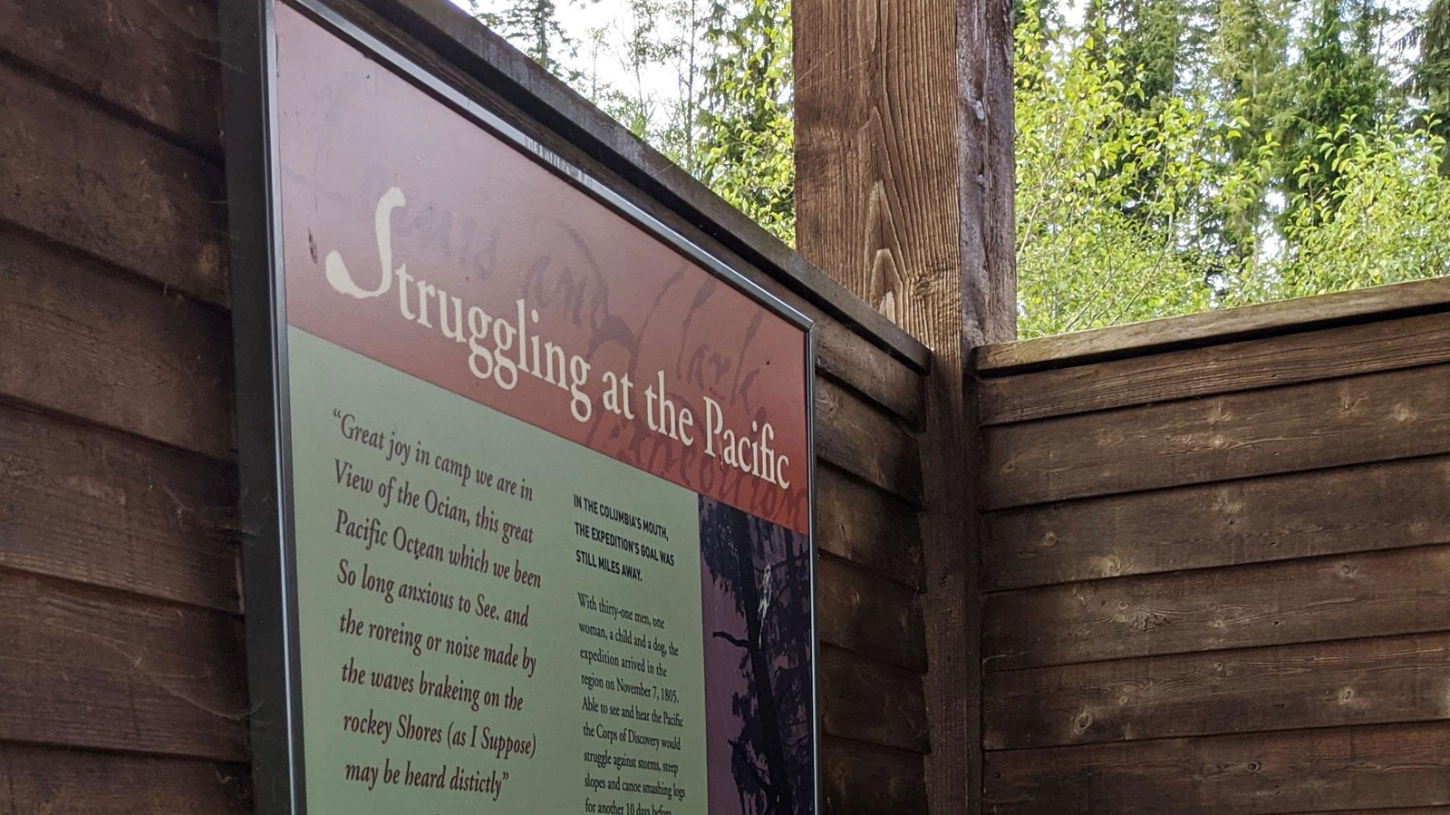 Wooden slats in an open air shelter support a large colorful sign with bold text, pictures, and maps