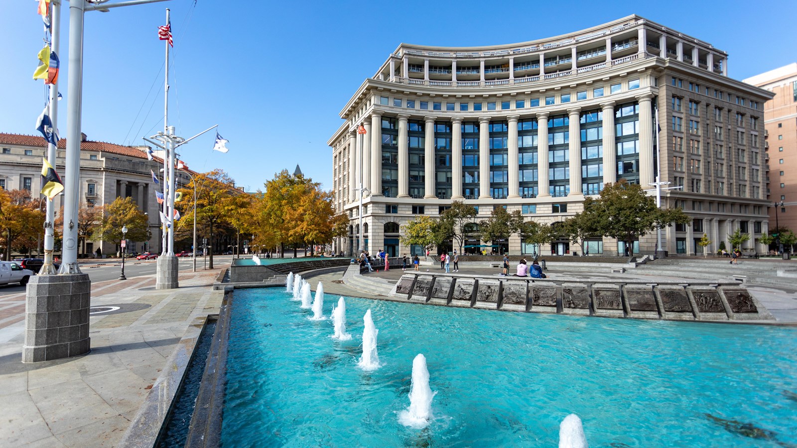 Fountains bubble upward in a blue pool. Flagpoles alongside the pool resemble ship masts with flags.