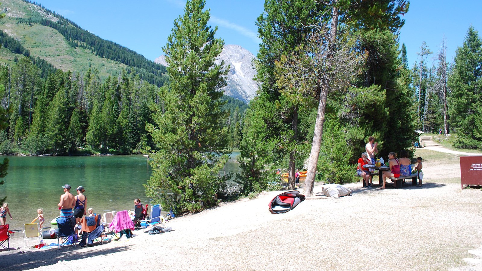 A couple different family groups sit along a lake and at a nearby picnic table.