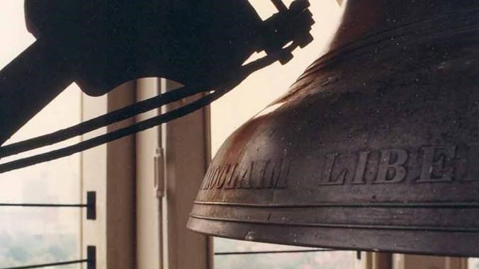 A hammer mechanism sits to the side of the base of a large bell in a tower overlooking city building