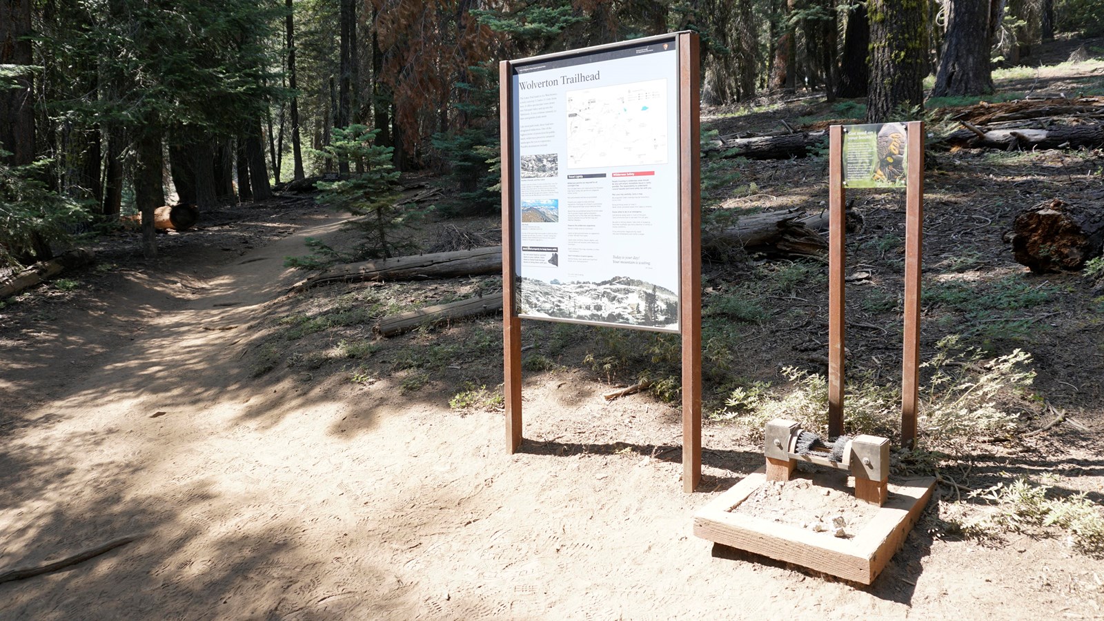 A metal framed sign with information about Wolverton stands in front of a shade covered trail