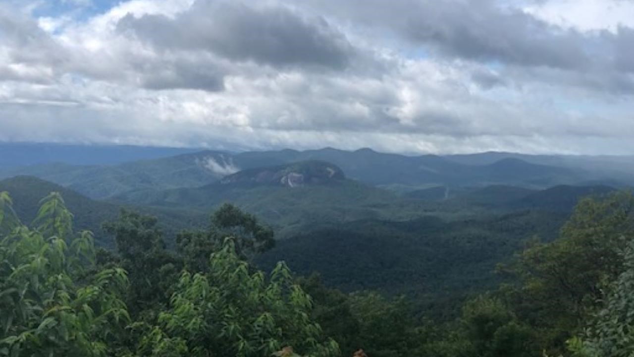Long range view of lush green mountains and Looking Glass Rock with blue sky and white clouds above.