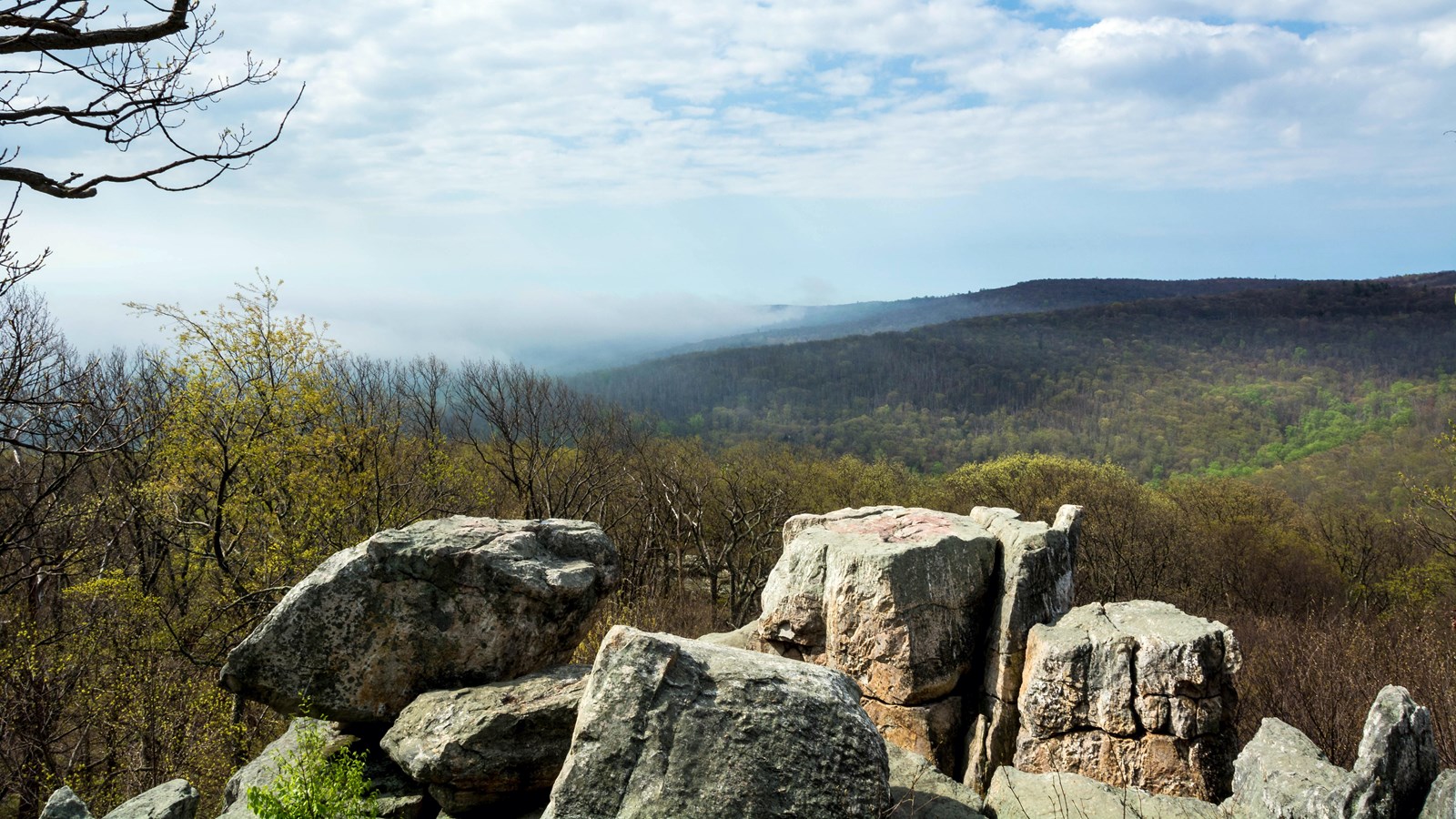 A jumble of large boulders is visible with a sweeping mountain view behind it.