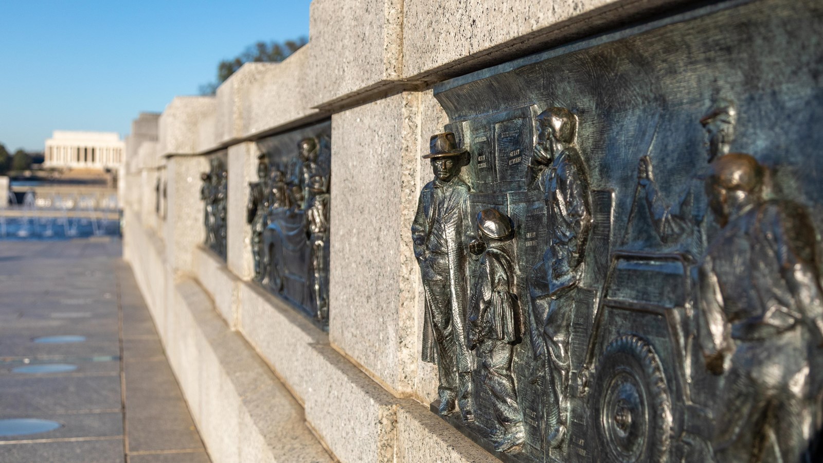 Bronze sculptures of scenes from World War II line a stone wall descending to a pool.