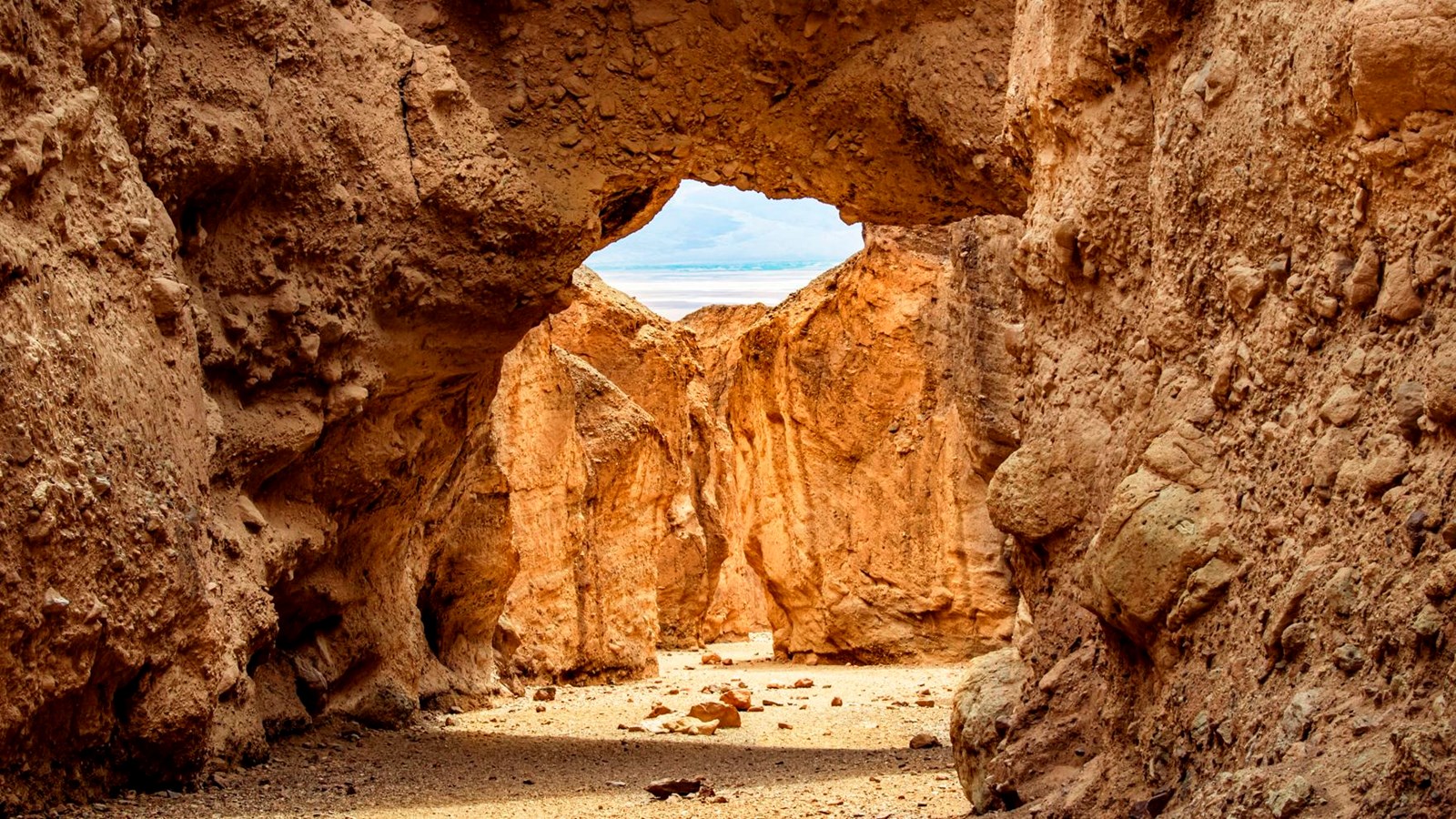 Vertical canyon walls with white salts flats in the distance seen from under a rock bridge formation