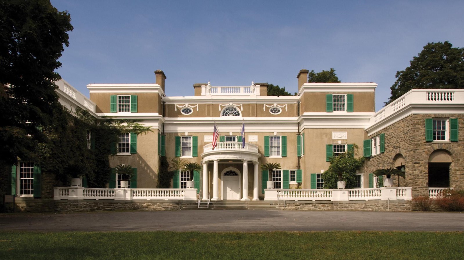 A classical house with two-story fieldstone wings flanking a central three-story stucco bay.