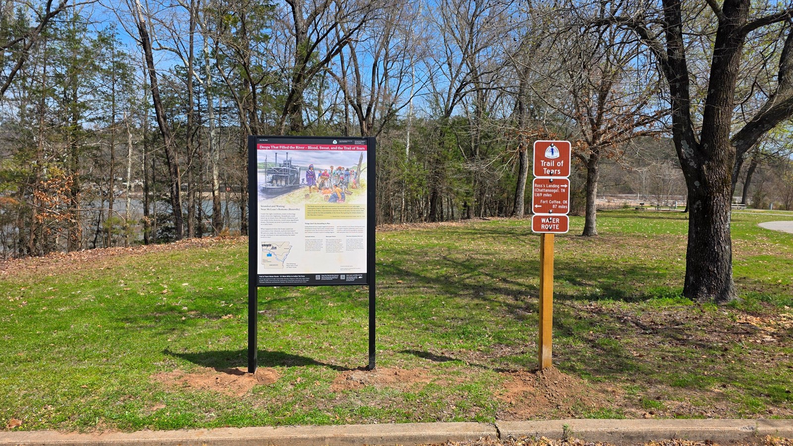 An upright wayside panel and Trail of Tears route signage stand next to a parking lot.