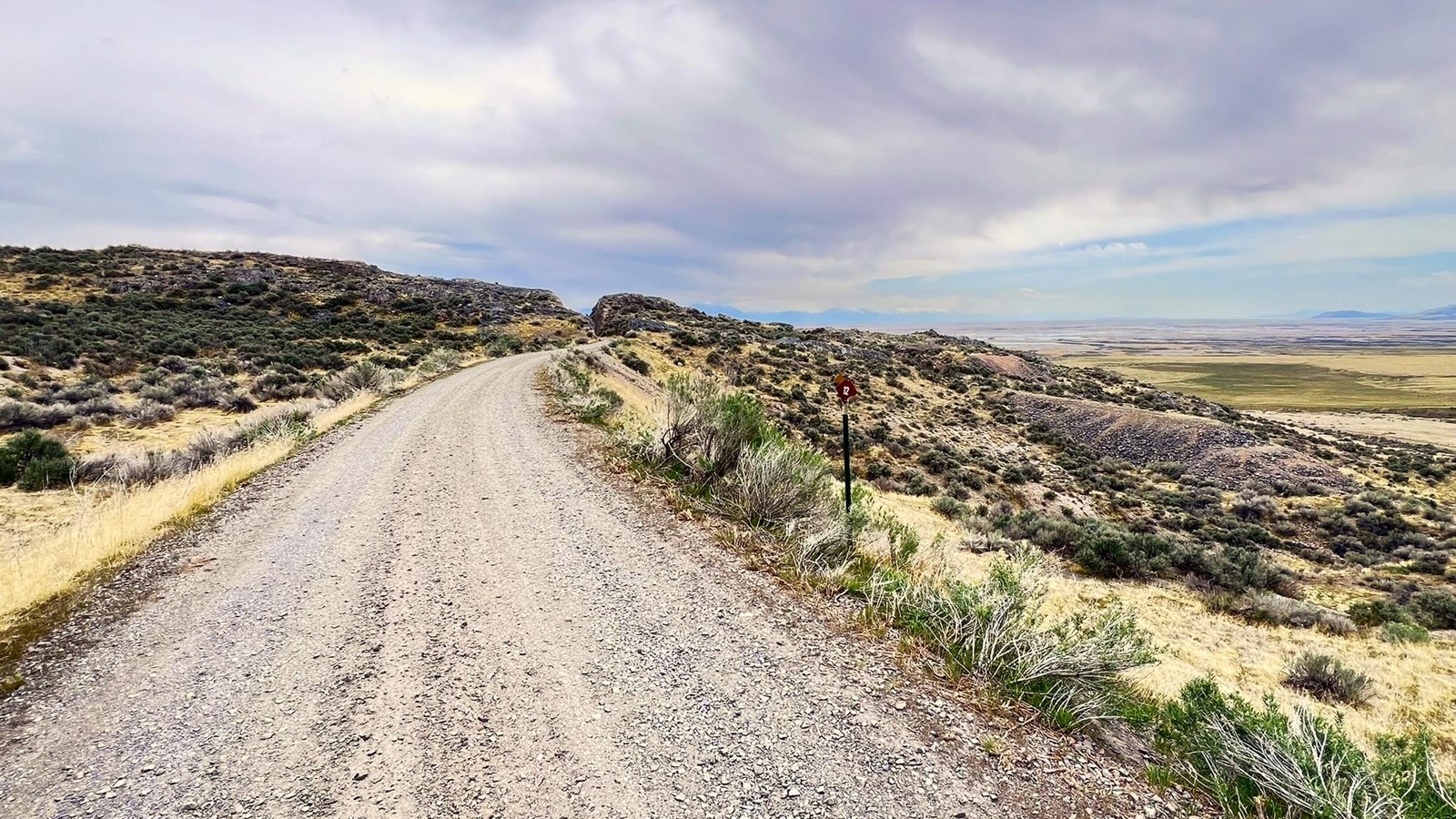 Gravel road among yellow and green sagebrush, views of vast valley mountains in distance
