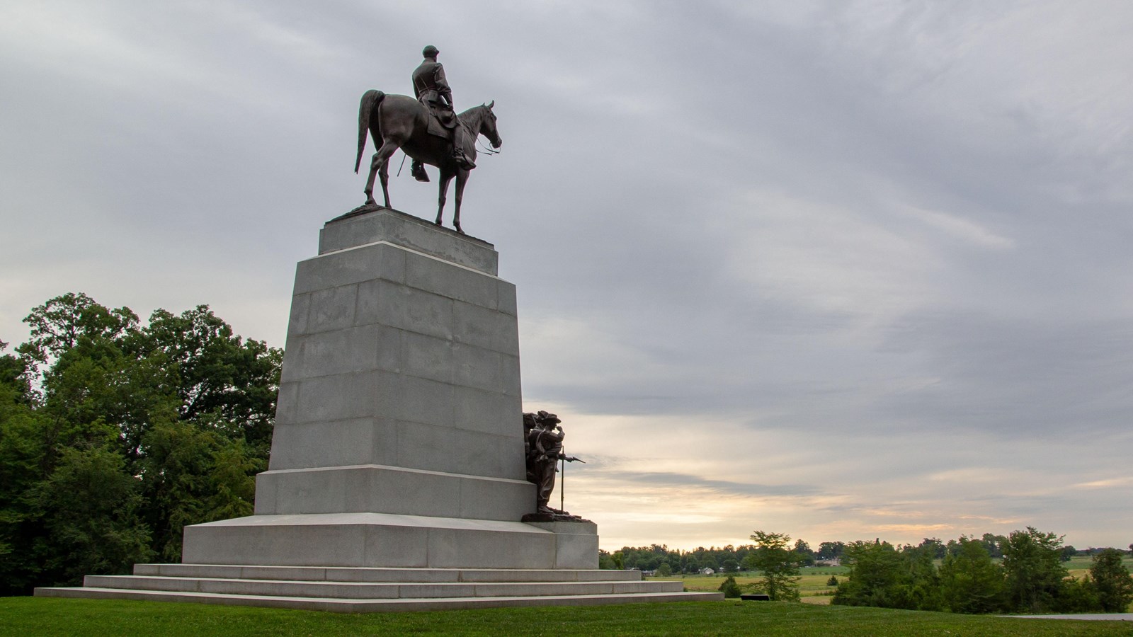 A large bronze equestrian statue on a marble pedestal with soldiers in bronze on the front. 