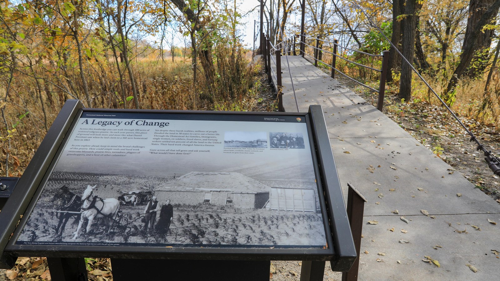 Yellow, green, and brown leaves surround a footbridge. An informational panel is seen in foreground.