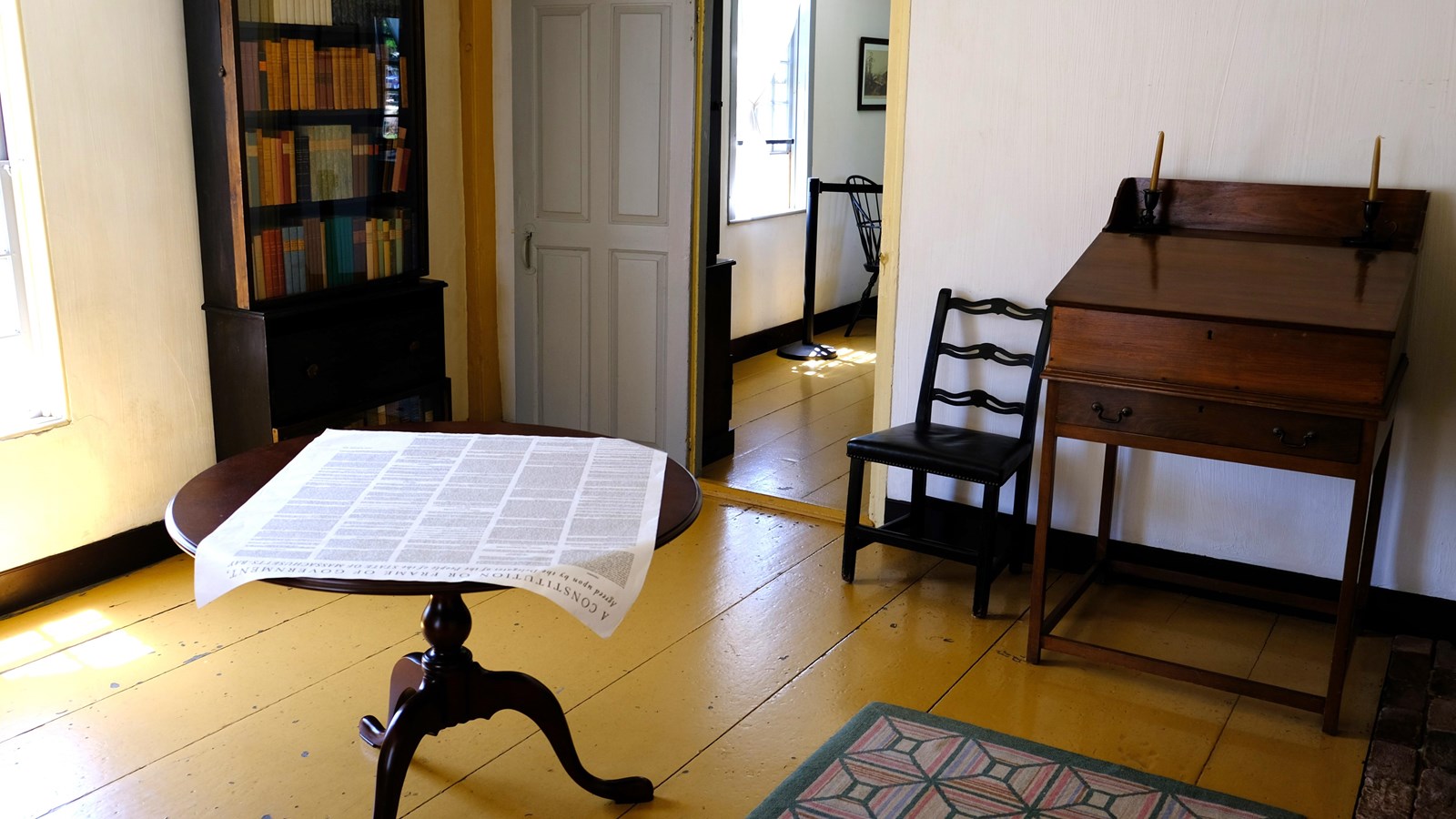 A plain room with a desk, chair, table, and bookcase.