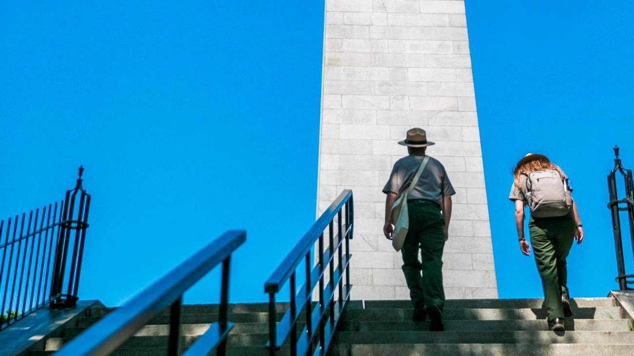 2 Rangers walking up a set of stairs to the Bunker Hill Monument. 