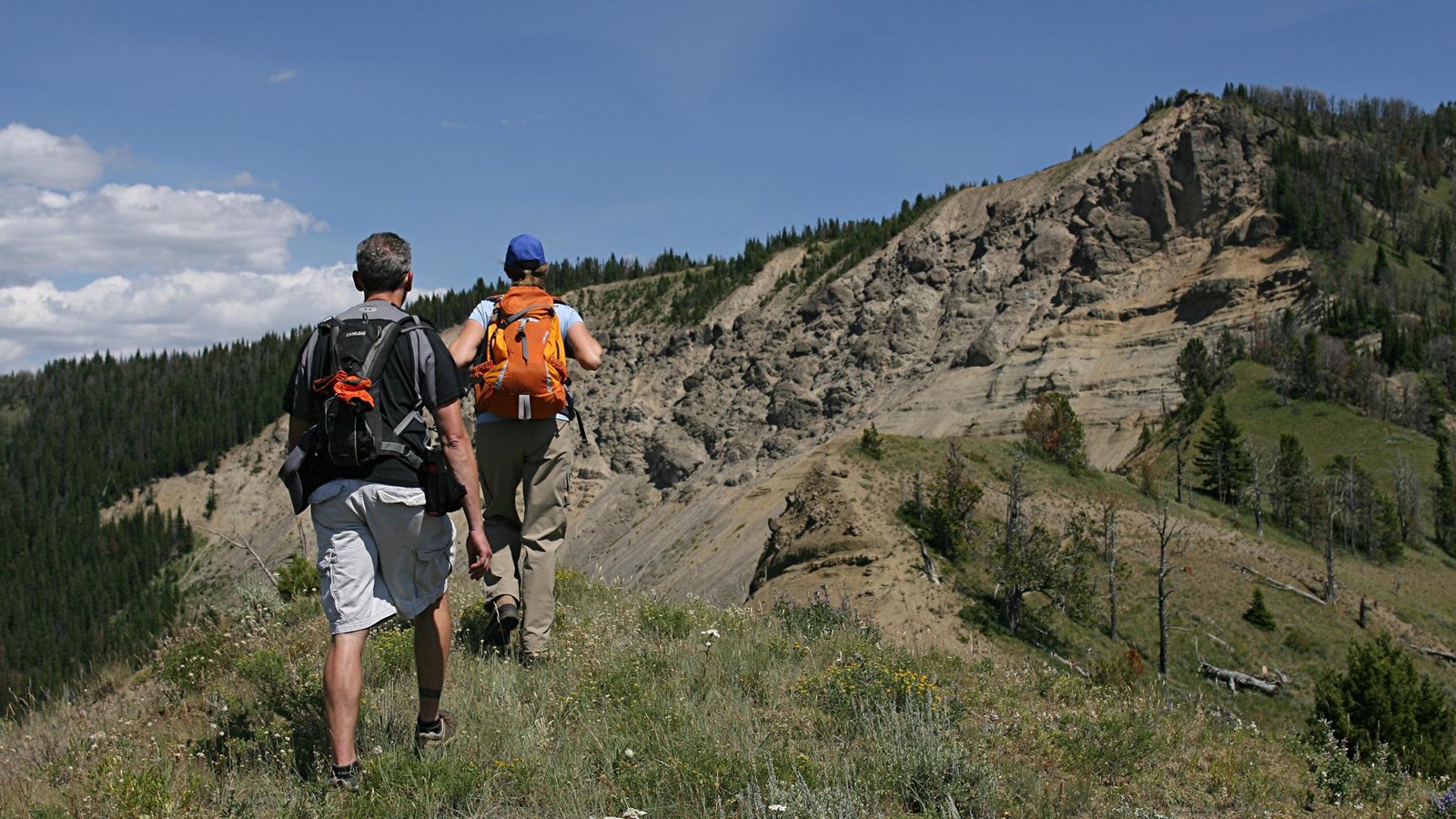 Two people walk along a slope towards a rocky outcropping.