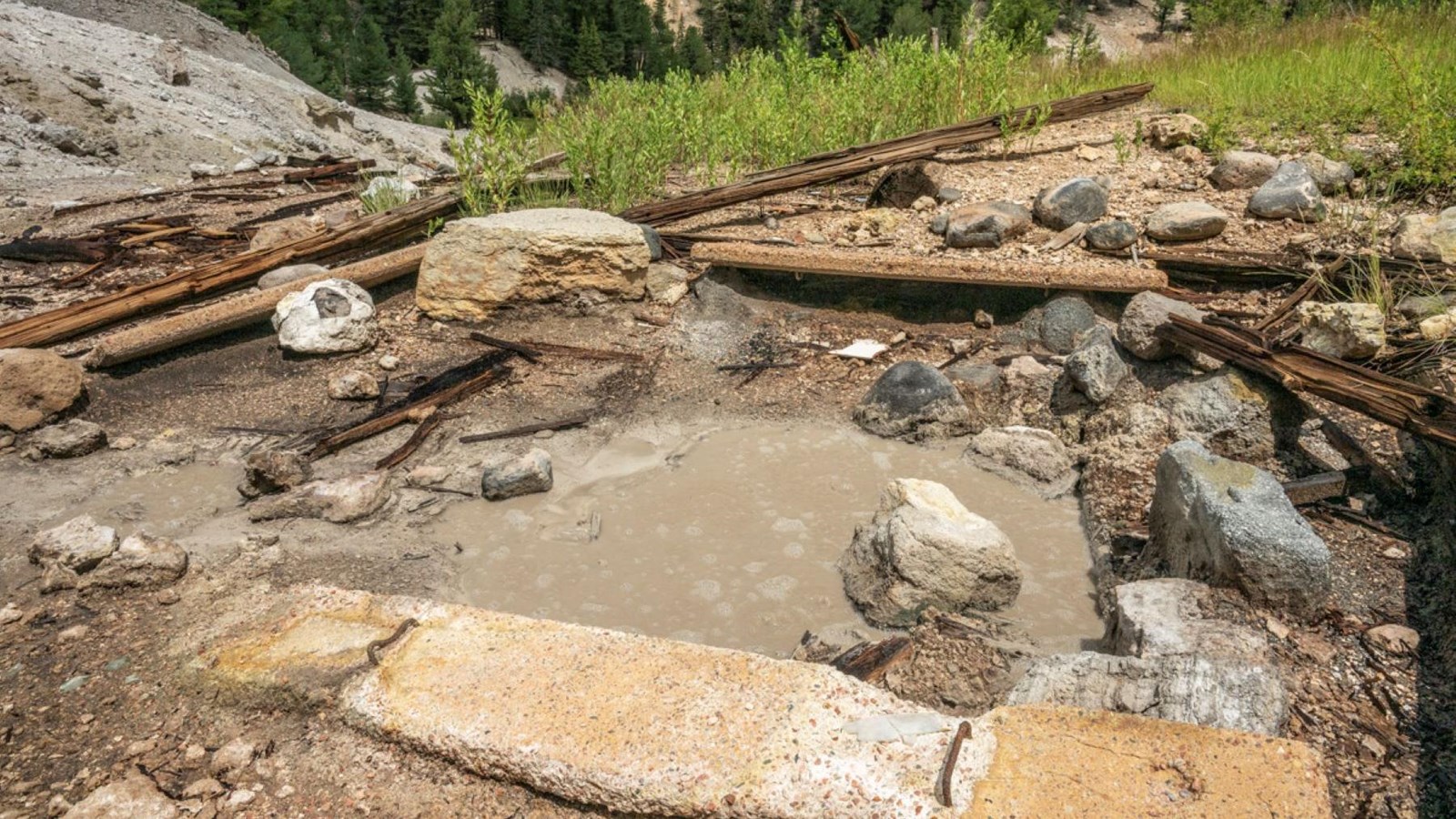 Remnants of an old structure around a bubbling pool of muddy water.