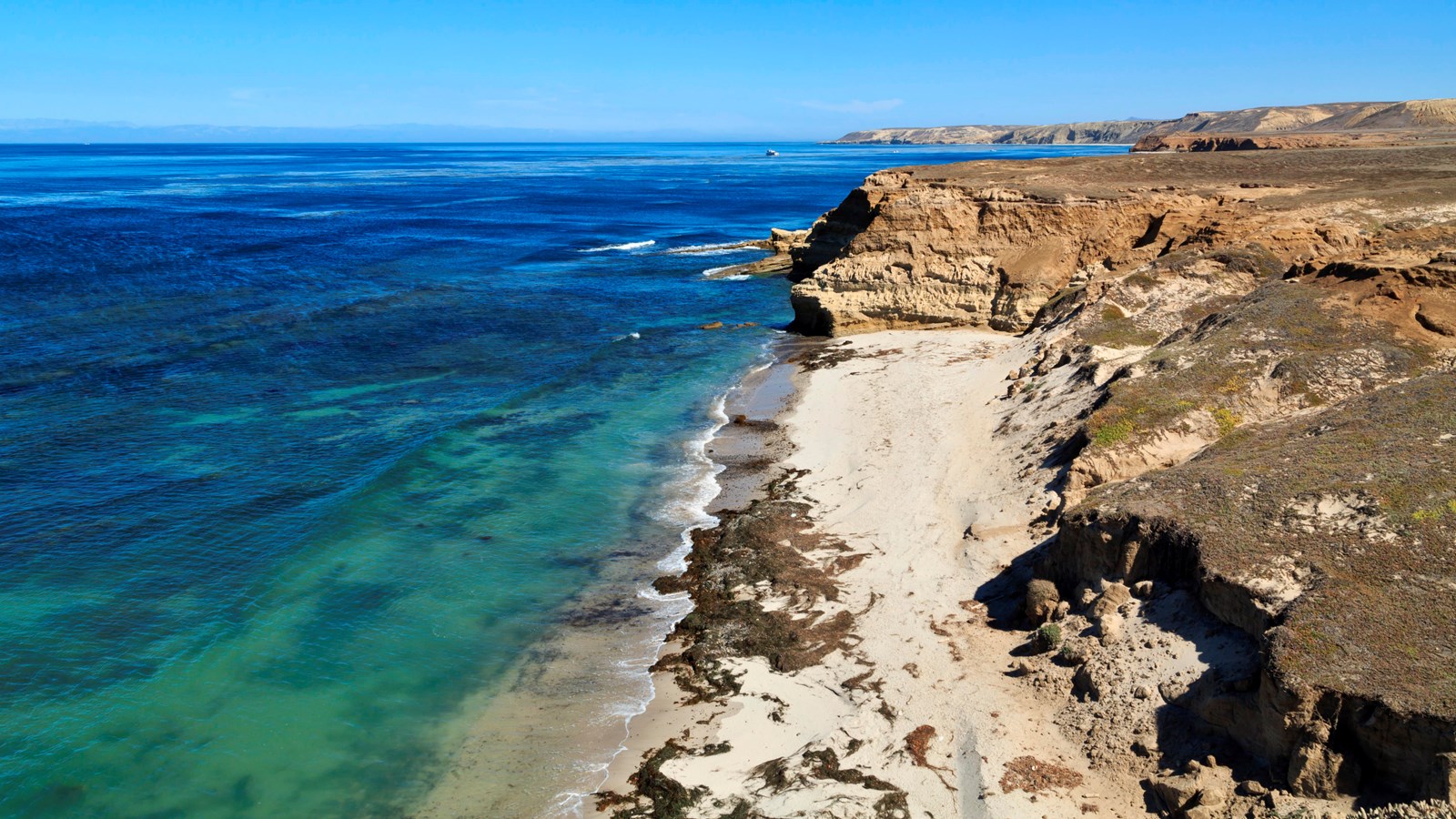 Low coastal mountains and terraces covered in dry grass leading to white sand pocket beaches and oce