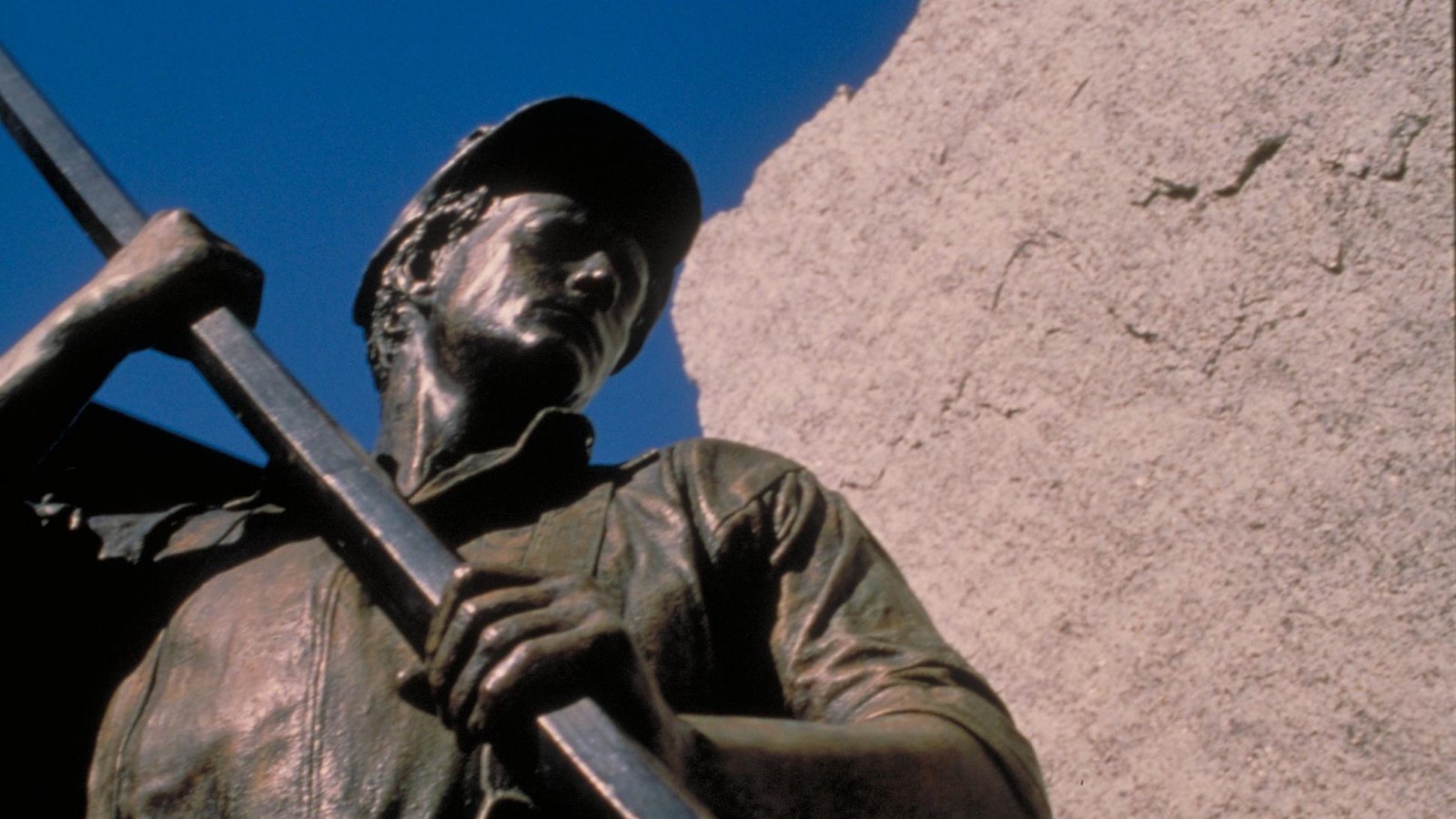 A sculpture of a man with a long metal tool moving granite blocks