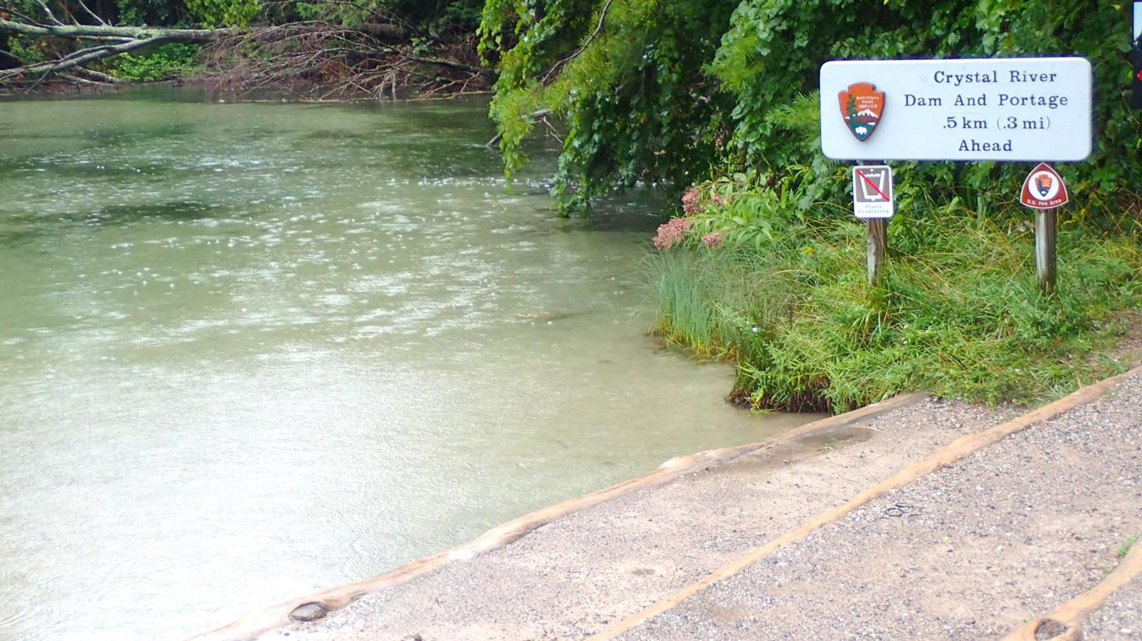 Light turquoise river flows by a stepped down gravel access area