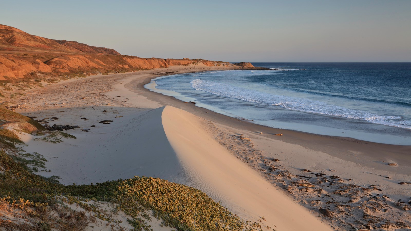 Low coastal mountains and terraces covered in dry grass leading to white sand beaches.