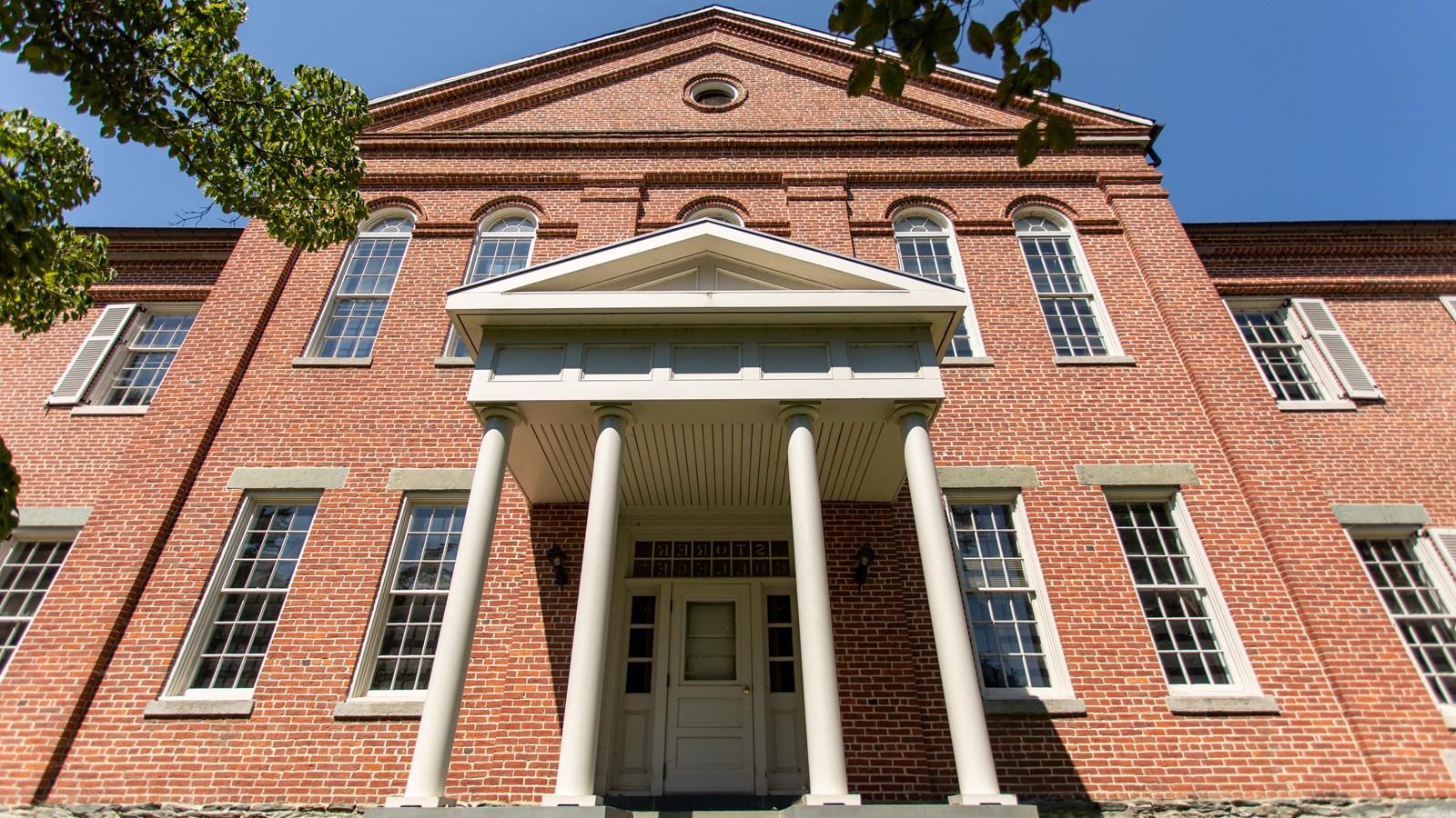 A brick facade of a building with 14 windows and an awning supported by four white columns.