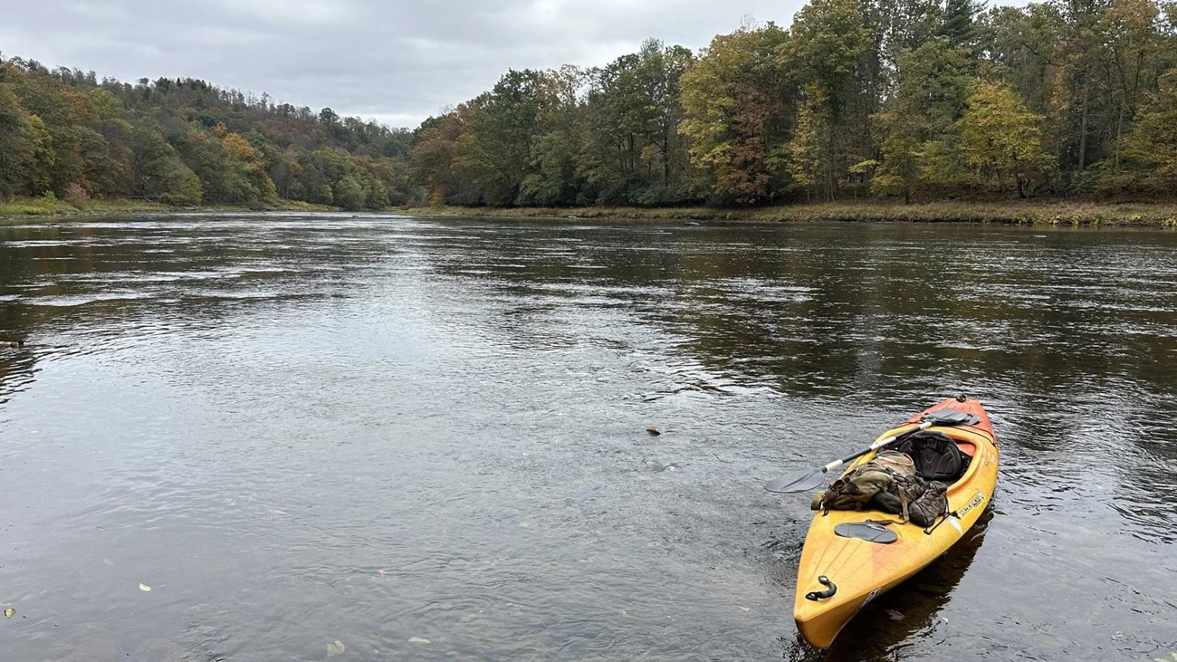 Yellow kayak on a calm river with wooded banks under an overcast sky.