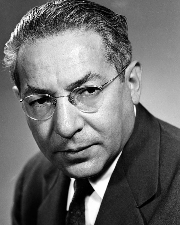 Black and white portrait of a man in a suit wearing rimless glasses.
