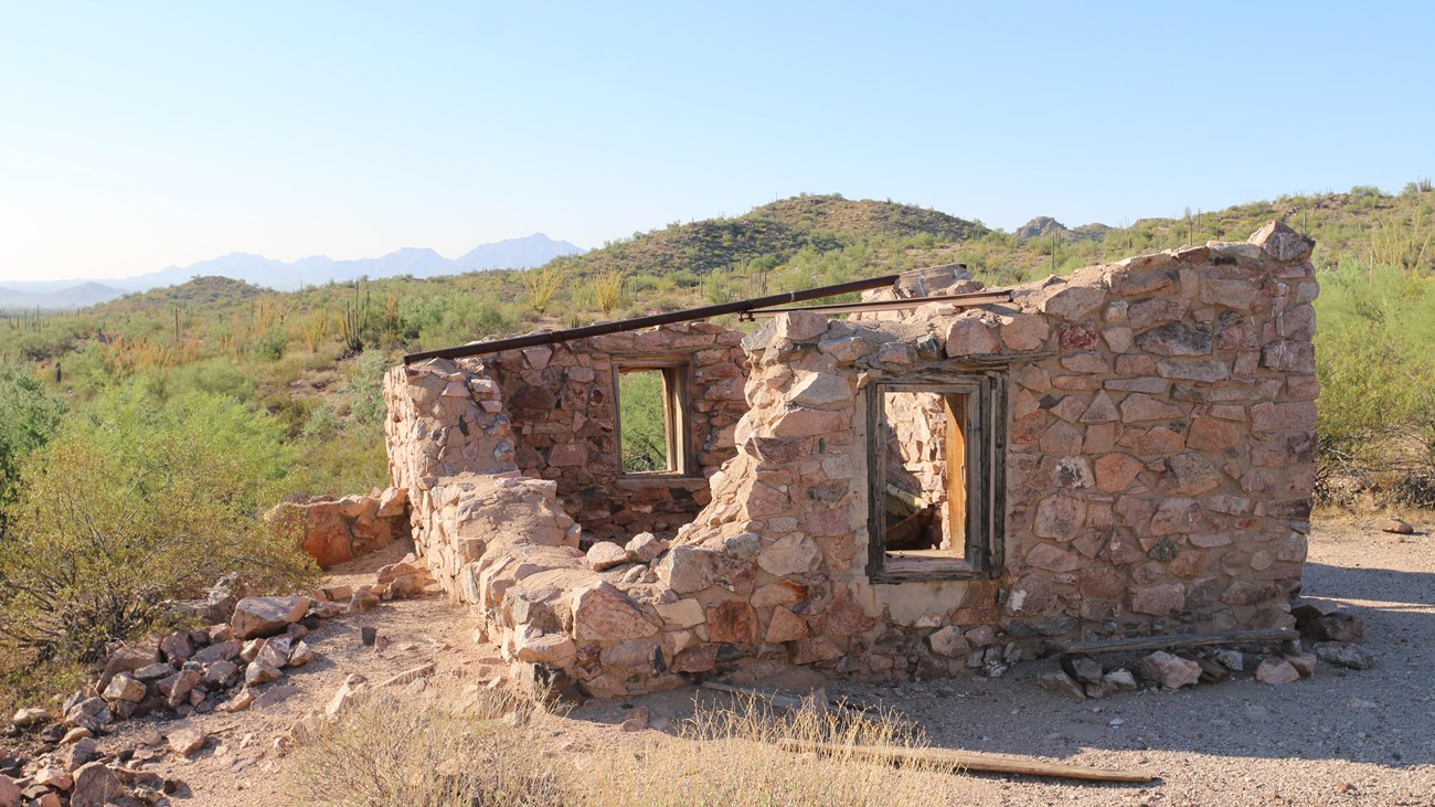 Historic one-room building made with stone walls and no roof, located in a desert.  