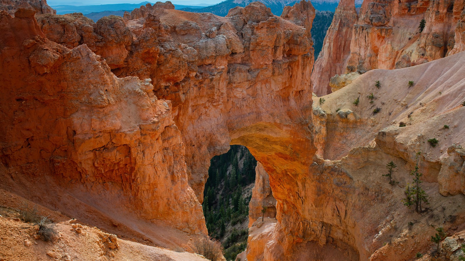 A glowing orange rock arch stands among limestone slopes above a forested landscape