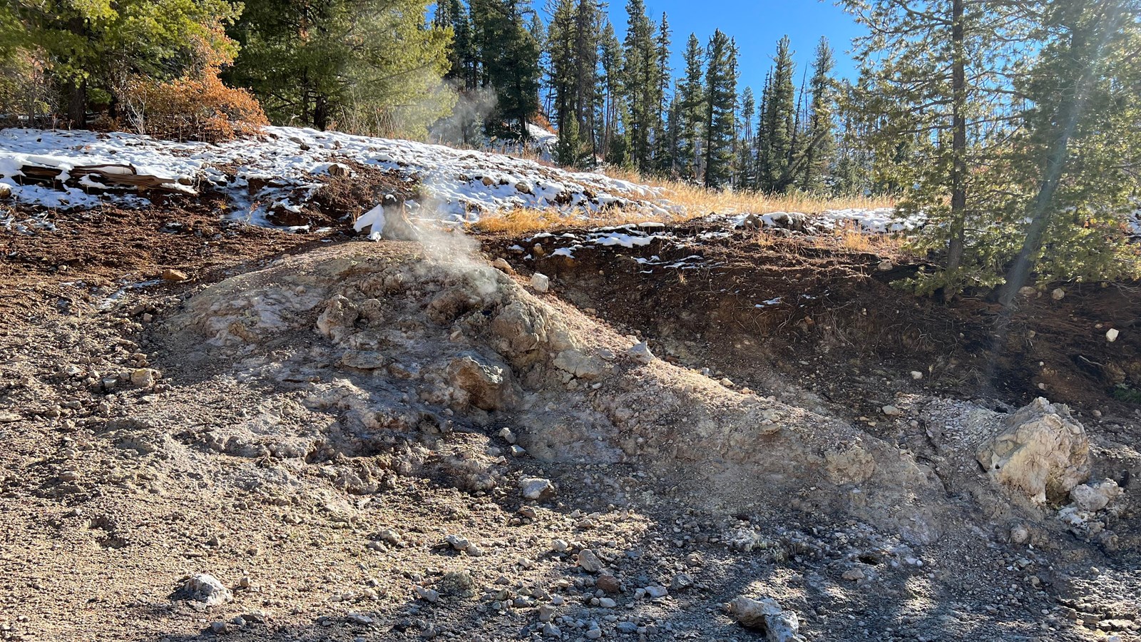 Steam rises from the ground composed of bleached rock and soil.